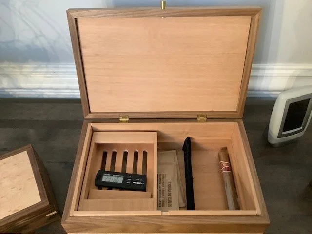 Open wooden box with various compartments, containing a digital device, a pen, and a cigarett