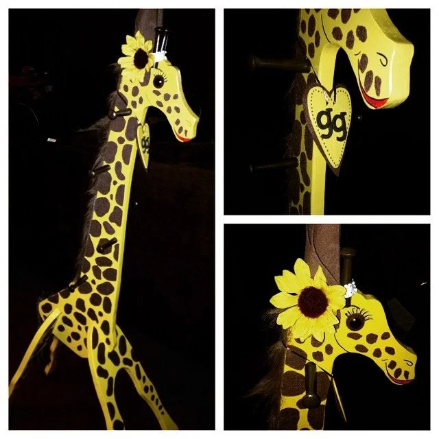 Decorative yellow giraffe with brown spots and black eyes, adorned with sunflowers and a heart-shaped ornament with 'gg' on it.
