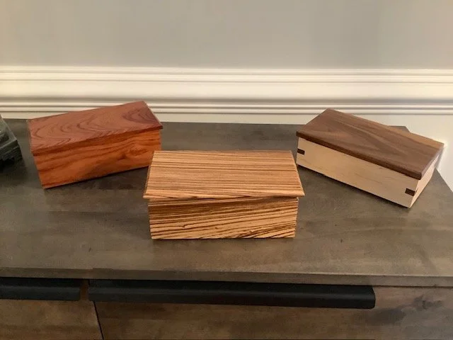Three wooden boxes with lids on a dark wooden surface against a light-colored wall.
