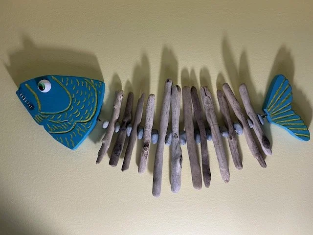 Wall decoration resembling a fish, made with painted wooden fish shapes for the head and tail, and driftwood arranged to mimic the body.