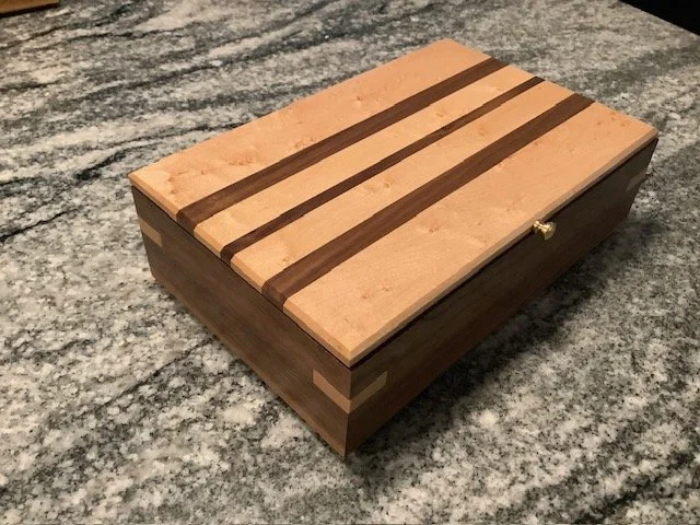 A wooden jewelry box with a sliding lid, placed on a granite countertop.