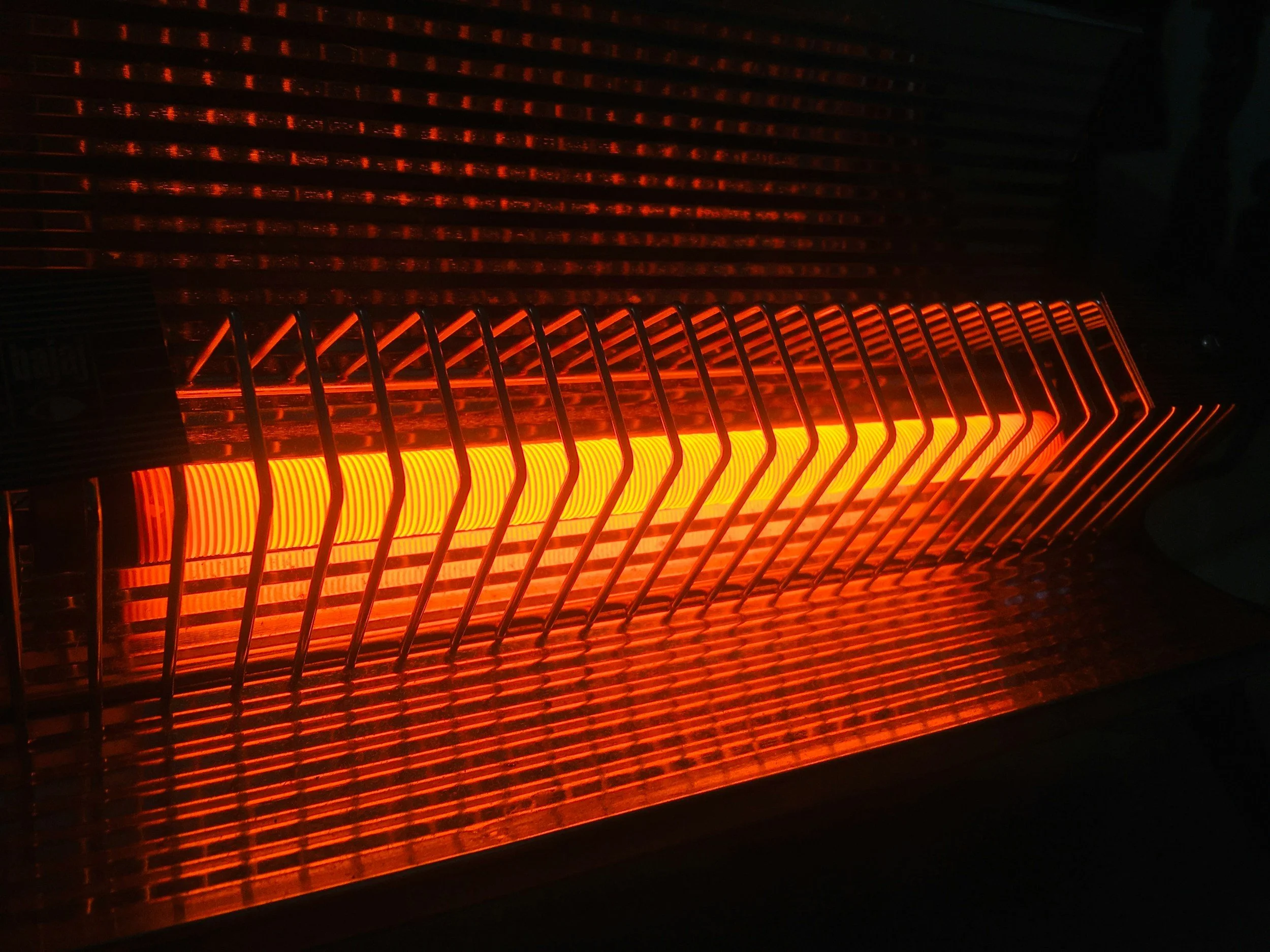 Un calentador de espacio con elementos de calefacción de luz roja, protegido por una rejilla metálica en un ambiente oscuro.