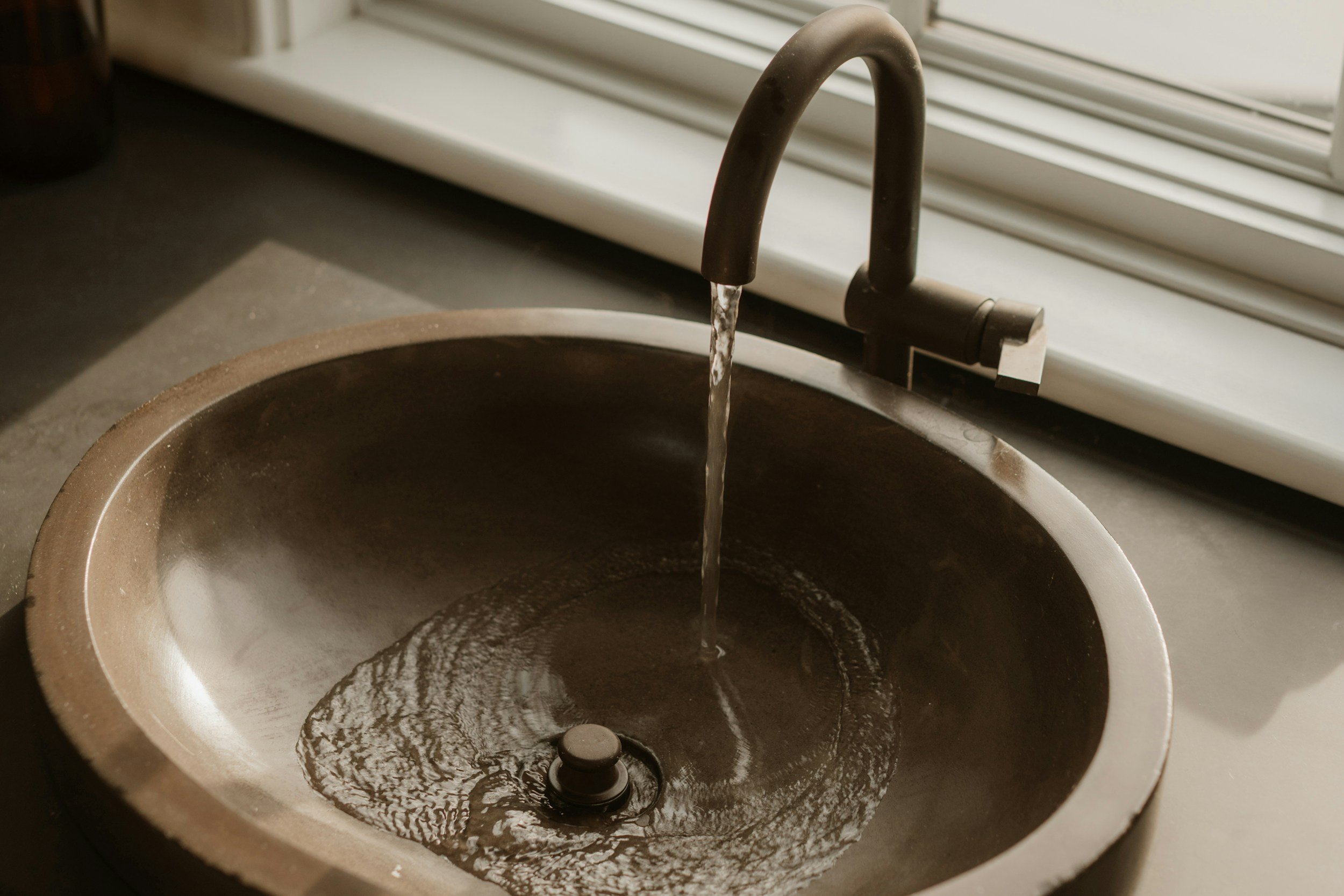 Grifo de cocina con agua fluyendo hacia un fregadero negro.