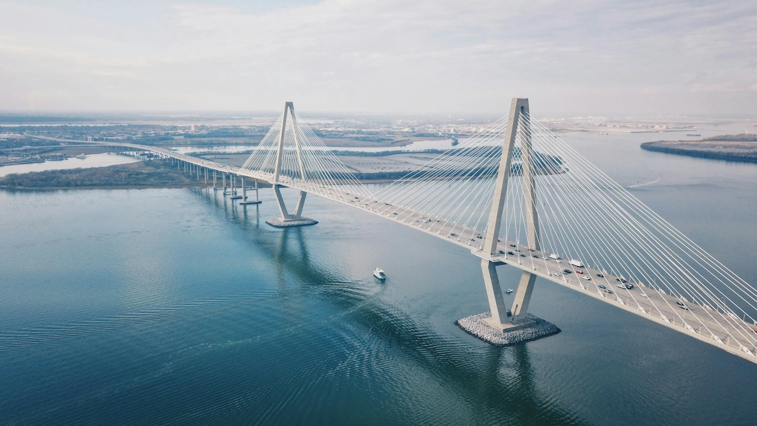 Aerial view of a modern cable-stayed bridge with tall pylons and multiple cables crossing a body of water, with cars traveling on the bridge.