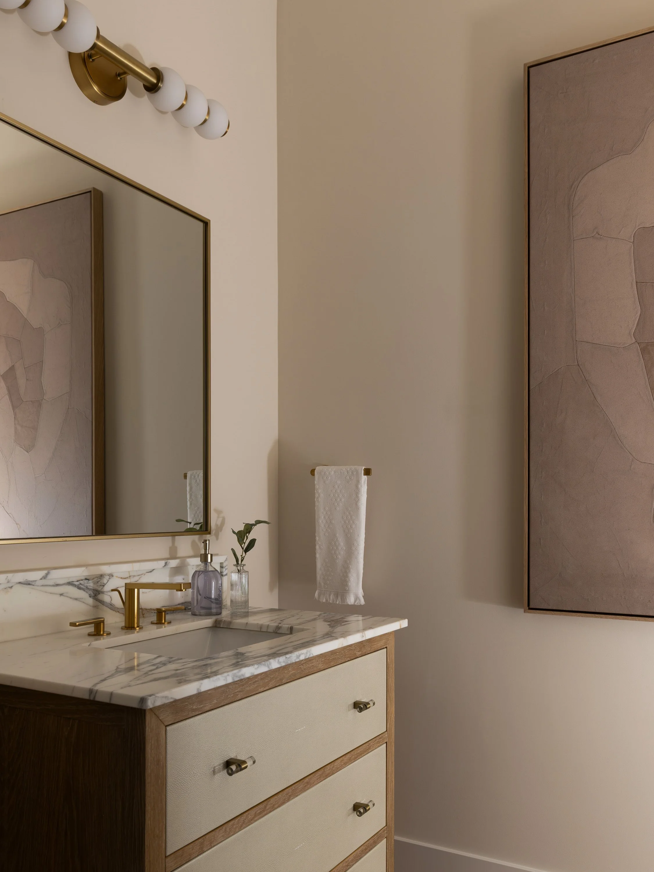 Bathroom vanity with a marble countertop, gold faucet, mirror, and a towel hanging on the wall.