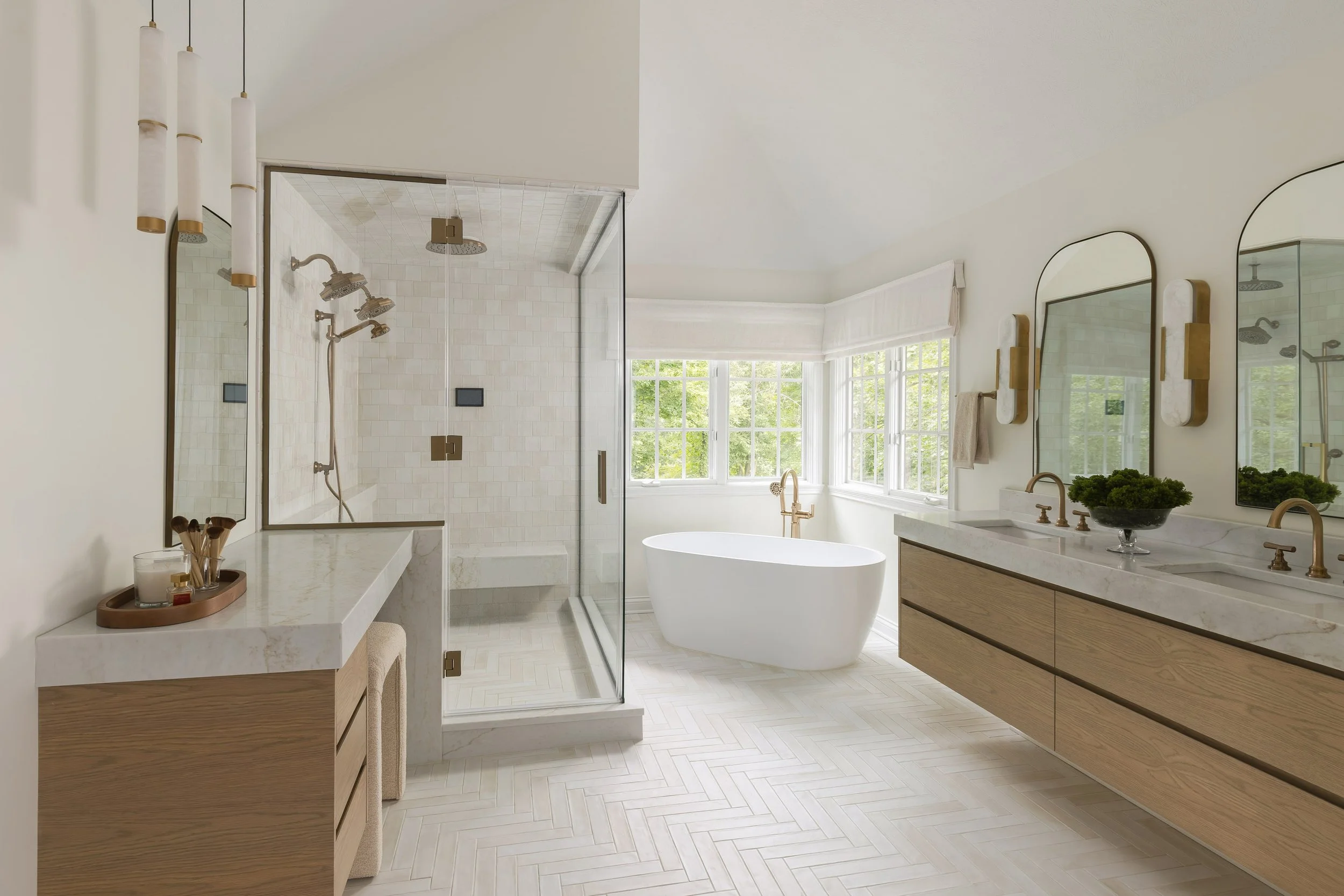 Modern bathroom with a walk-in shower with glass doors, three showerheads, a freestanding bathtub, large windows, a wooden vanity with a marble countertop, and decorative lighting.
