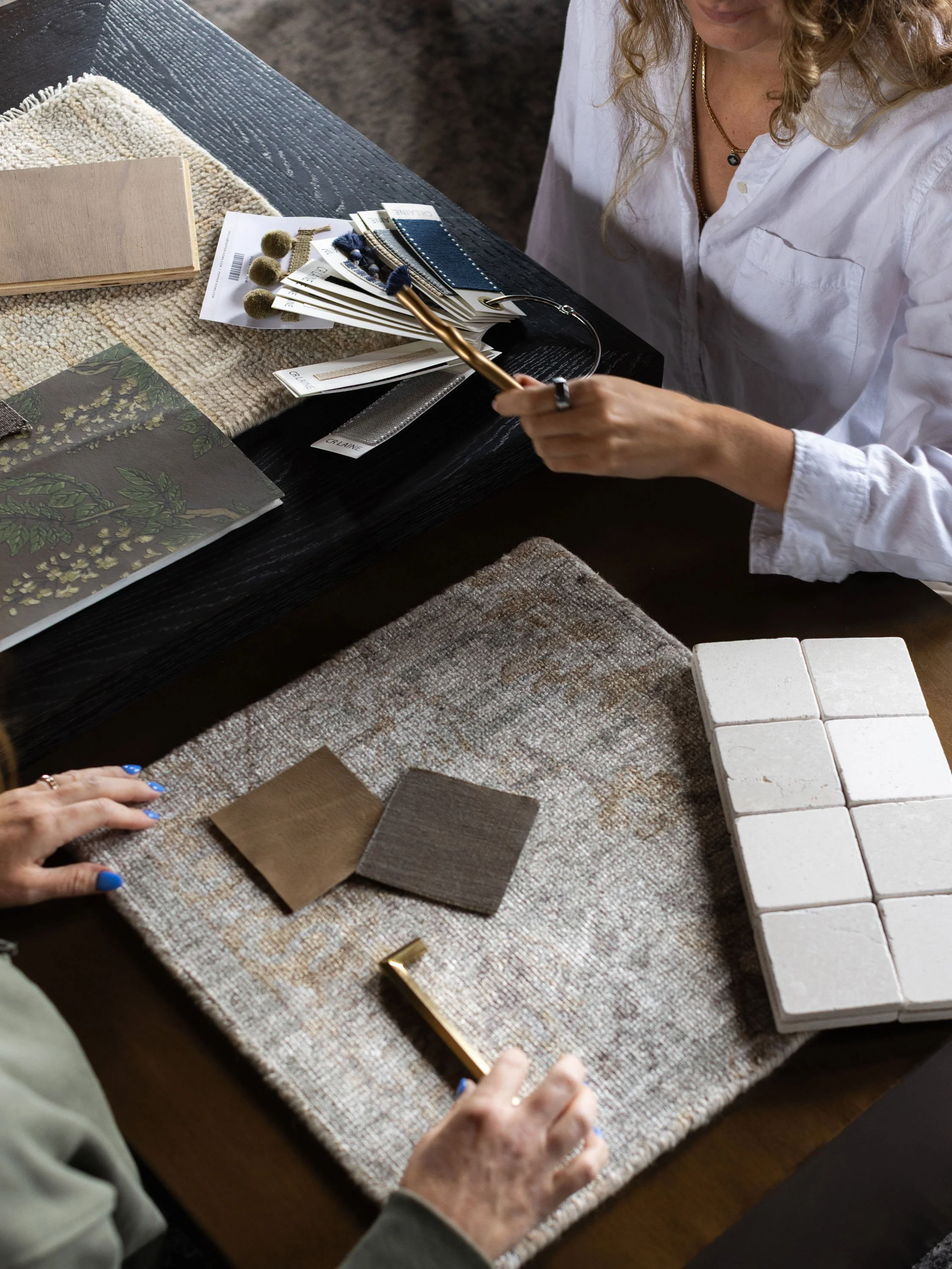 A person with curly hair and a white shirt looking at fabric and color samples on a table.