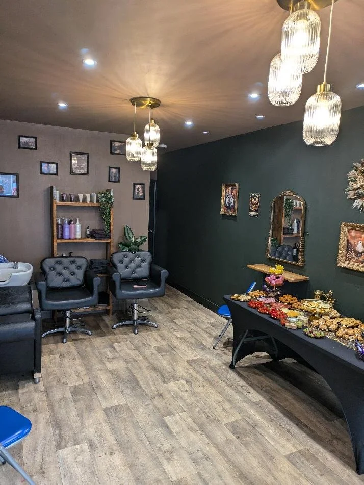 Panoramic view of an eclectic hair salon interior featuring styling stations, dark decor and a hair-washing basin in the corner