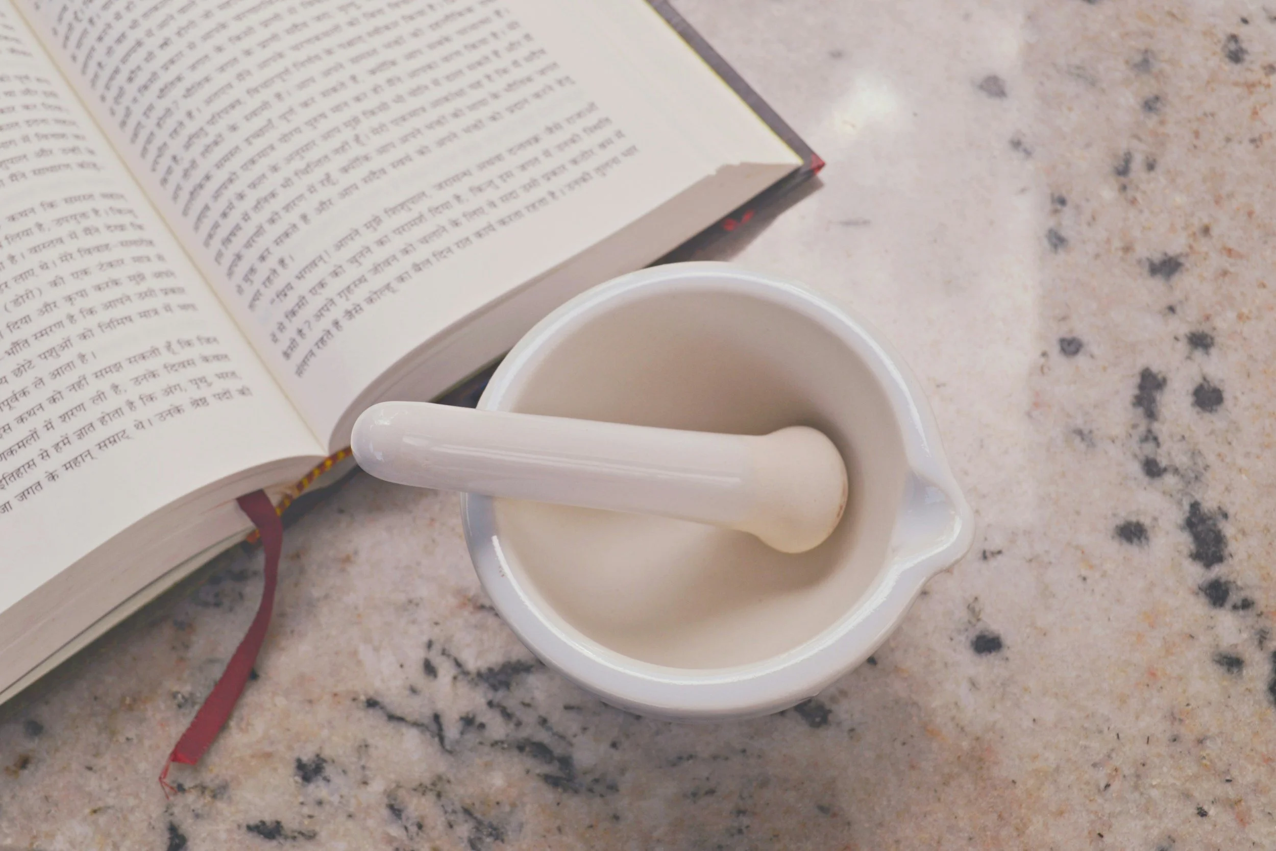 Open book with text, white mug with a spoon, on a speckled countertop.