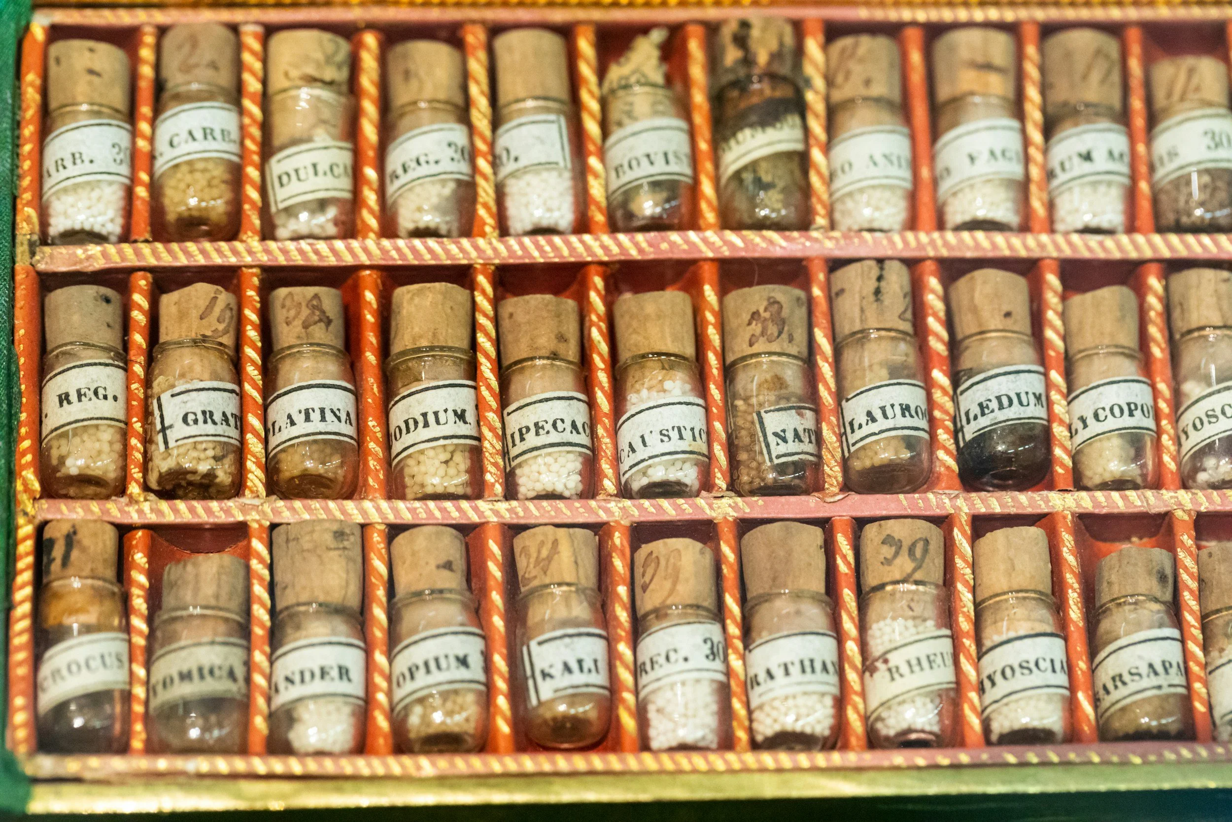 A collection of small glass jars with cork stoppers, filled with various spices, organized in a vintage wooden box with labeled compartments.
