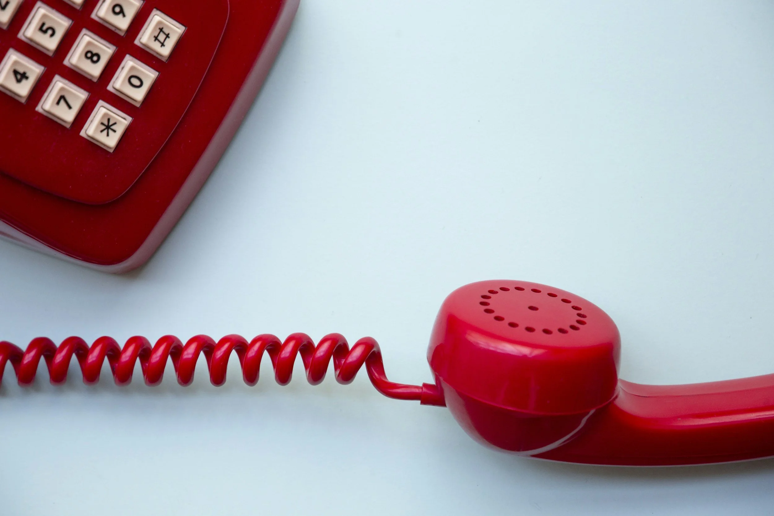 Close-up of a red vintage rotary telephone with a coiled cord, placed on a light-colored surface.