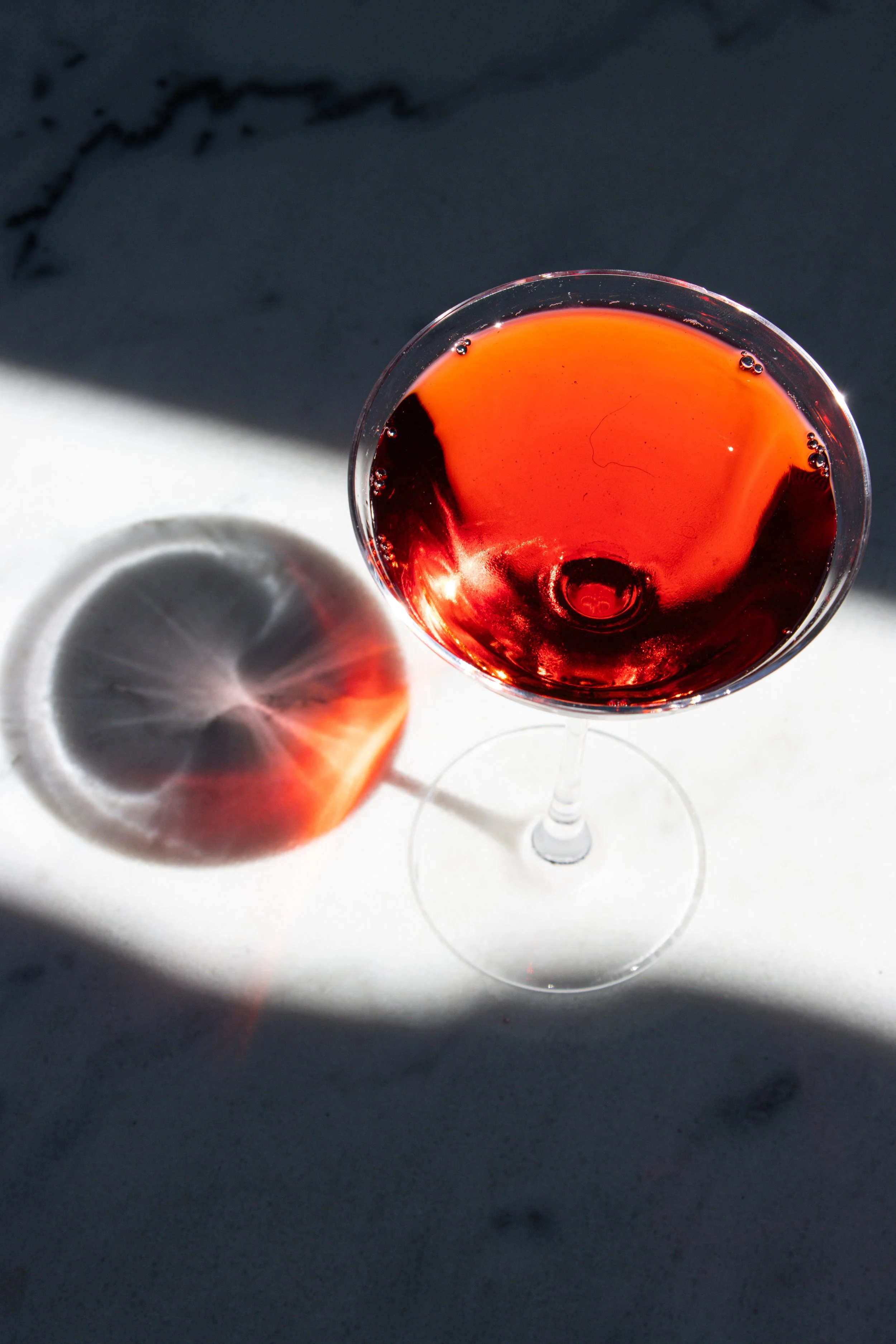 Un calice di vino rosso su una superficie bianca con una luce forte che crea un'ombra e riflessi.