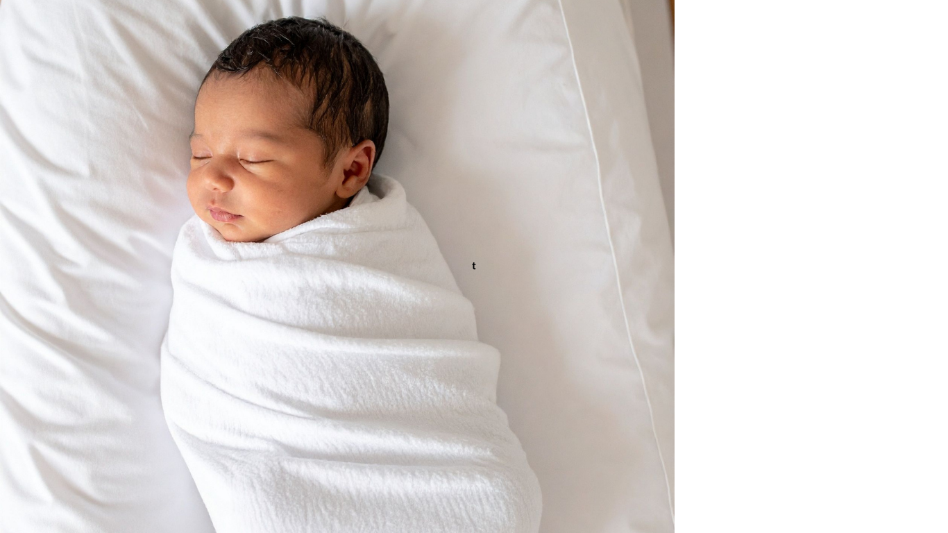 A sleeping baby wrapped in a white blanket, lying on a white surface.