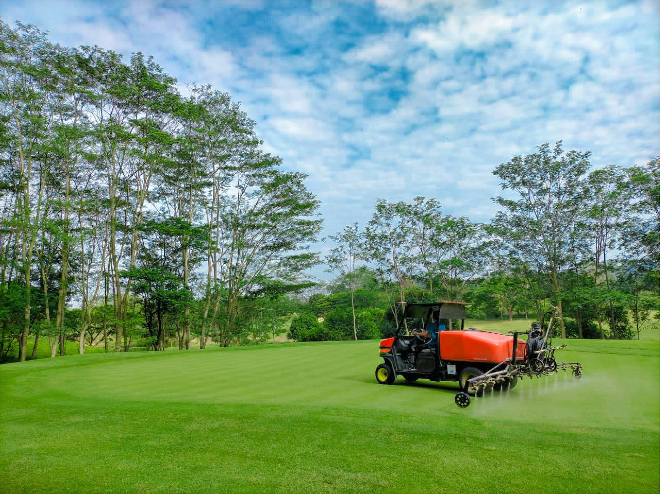 A golf course with lush green grass, trees in the background, and a piece of turf equipment treating the green.