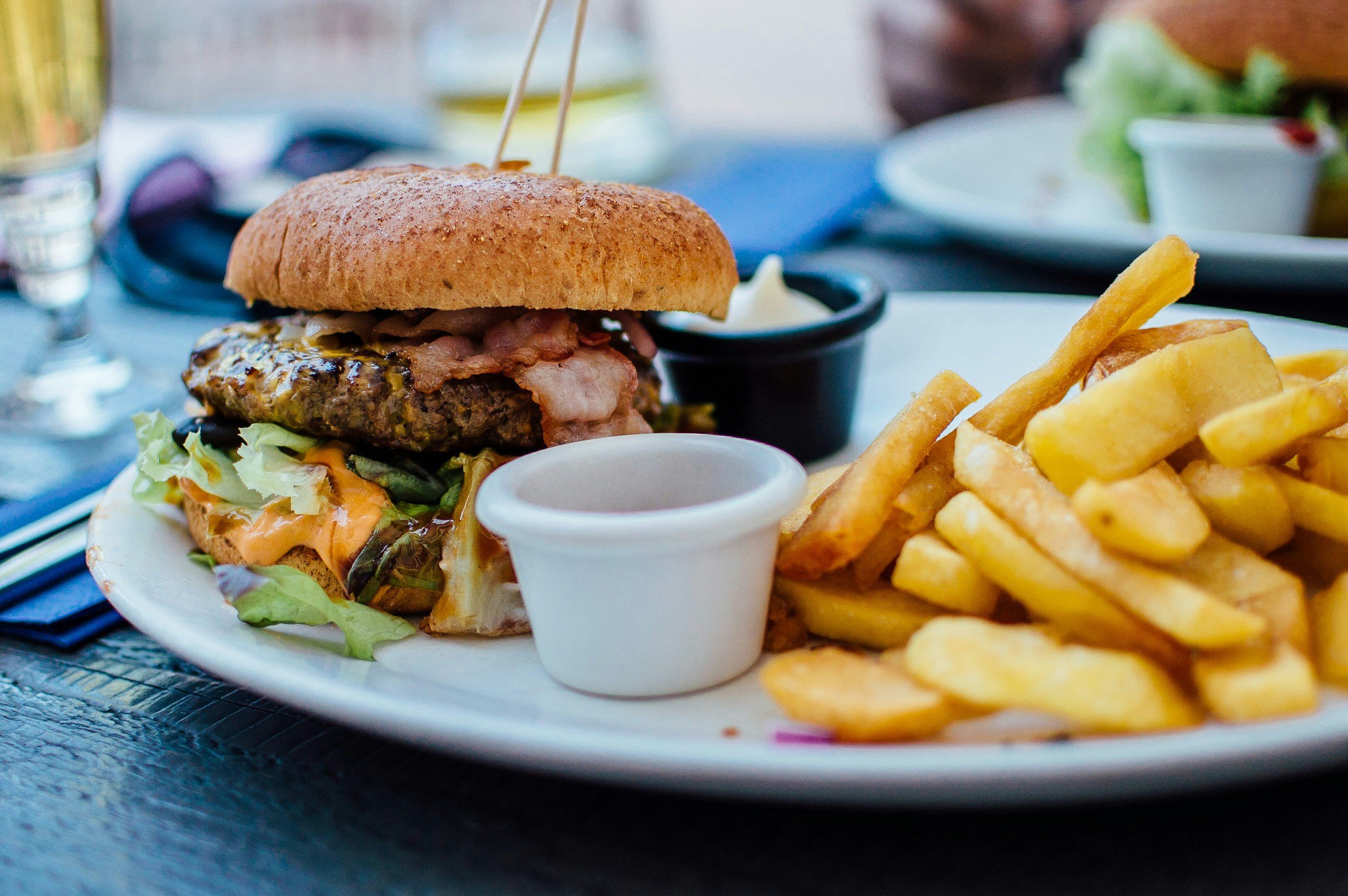 Plate with a cheeseburger, French fries, and small cups of dipping sauces on a table.