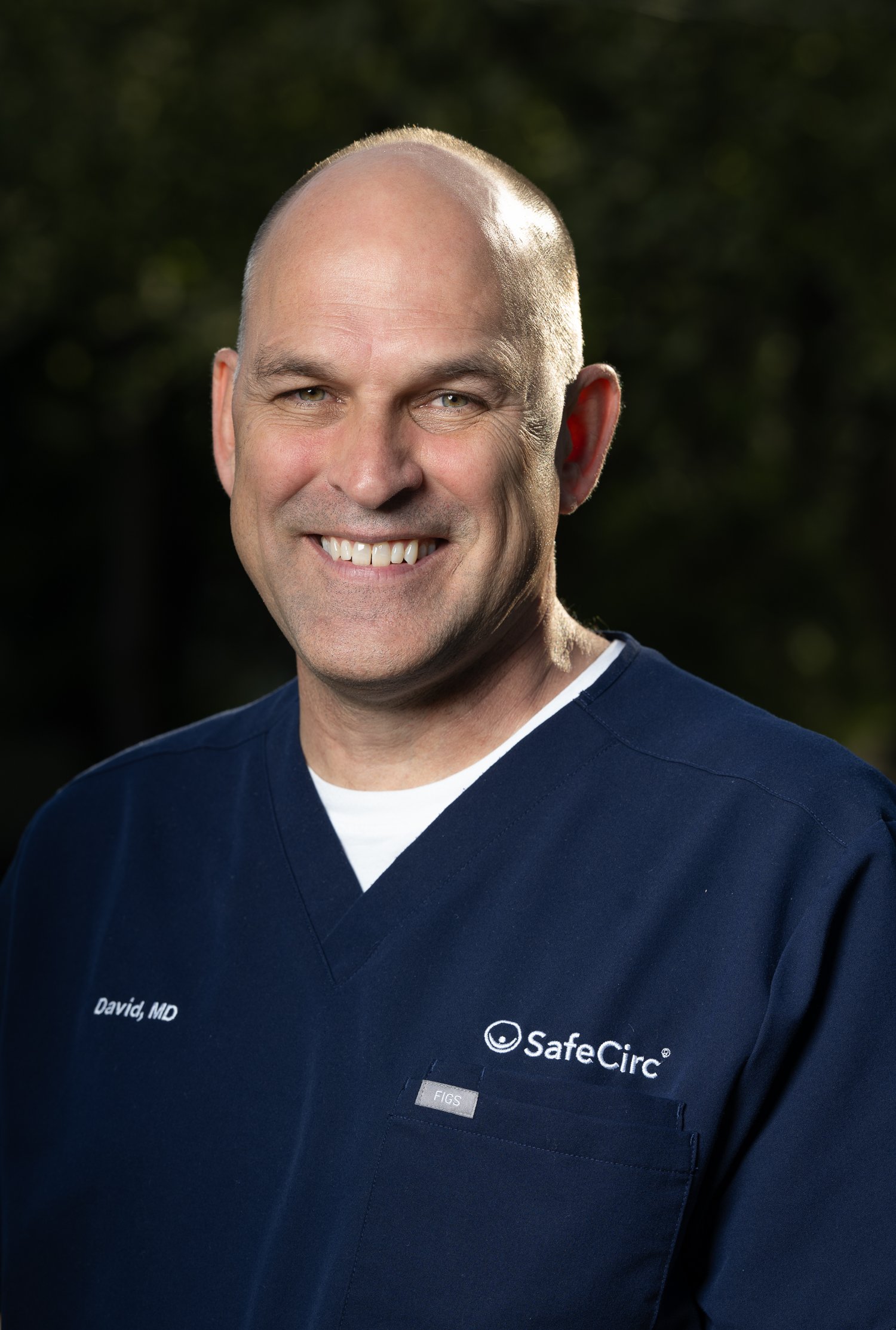 Headshot of a Dr Tomlinson wearing a navy blue medical scrub top with SafeCirc logo