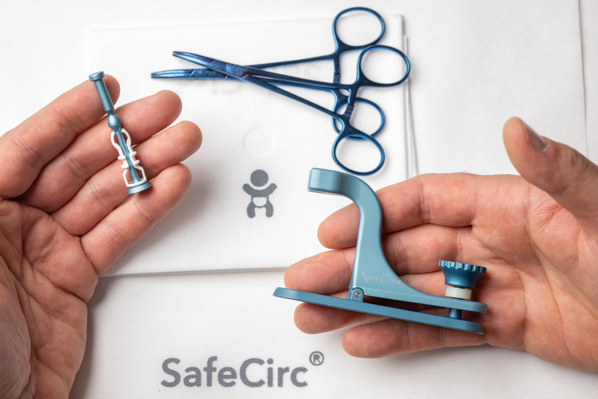 Person holding a small blue medical device or component with surgical scissors and a syringe on a white surface with the SafeCirc logo.