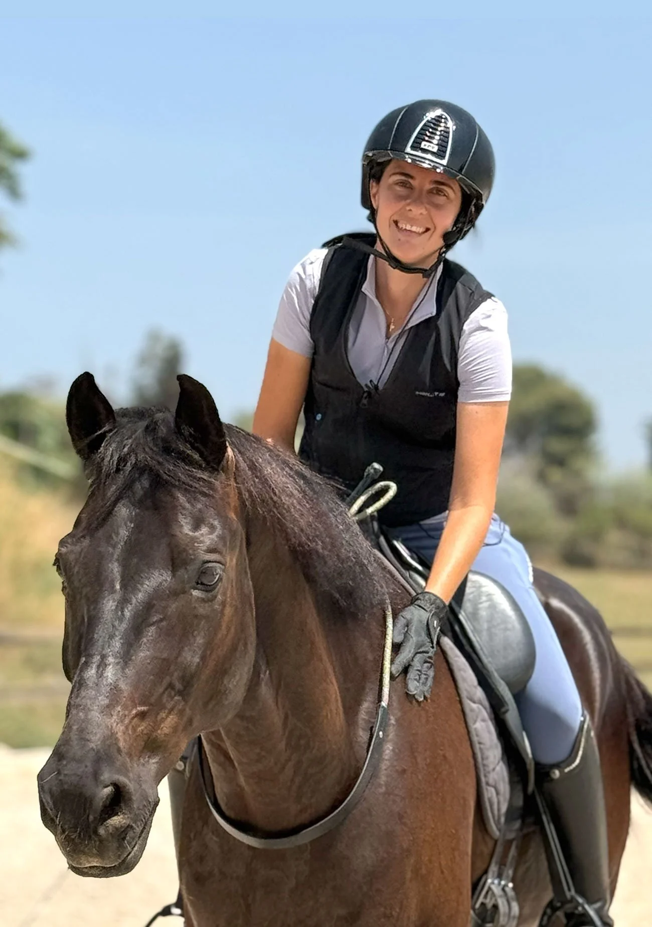 Arianna Saura Llopart sonriendo montando a su caballo de 14 años Oldenburgo Sandrino , lleva casco y chaleco en un día soleado.