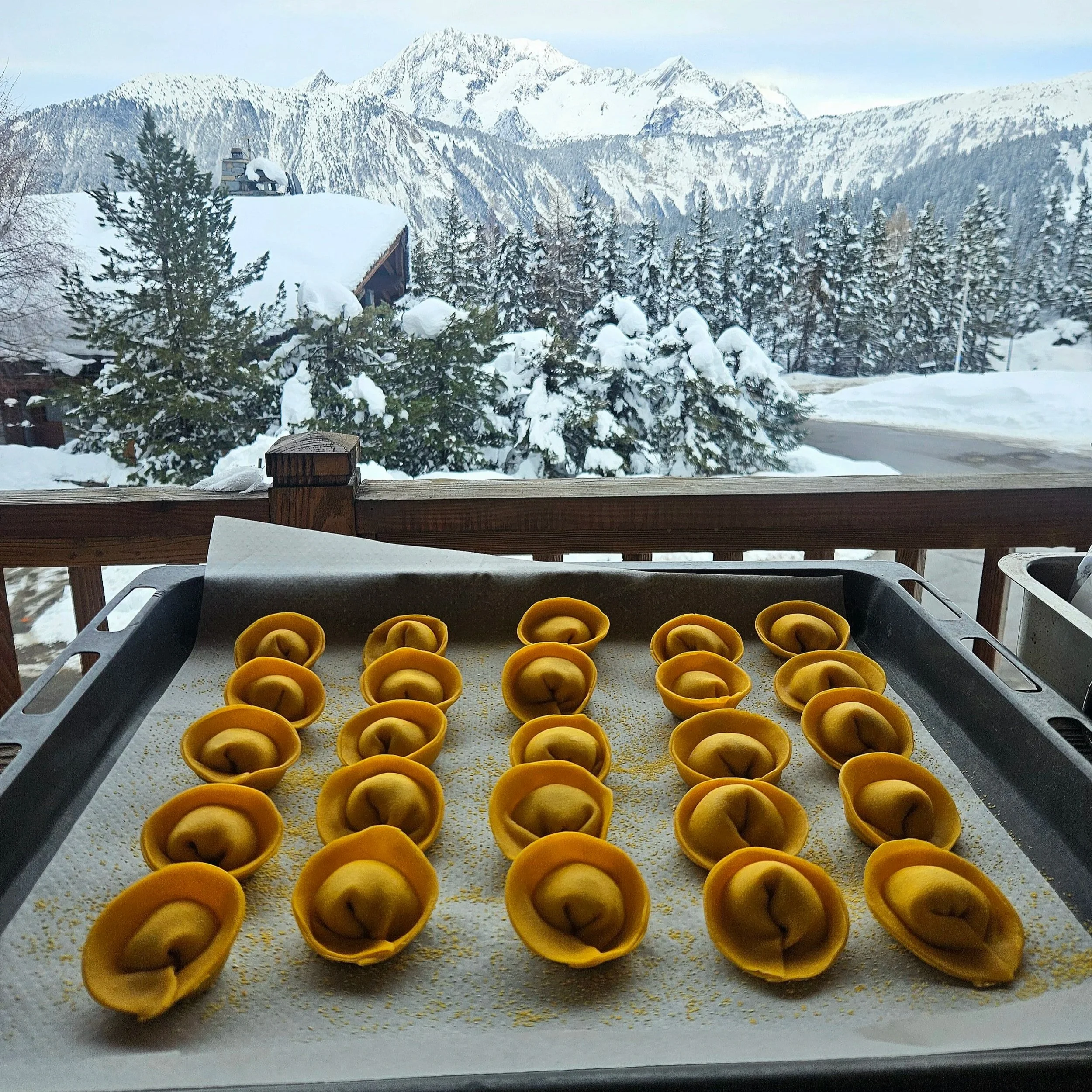 Tray of uncooked tortellini pasta with snowy mountain landscape in the background.