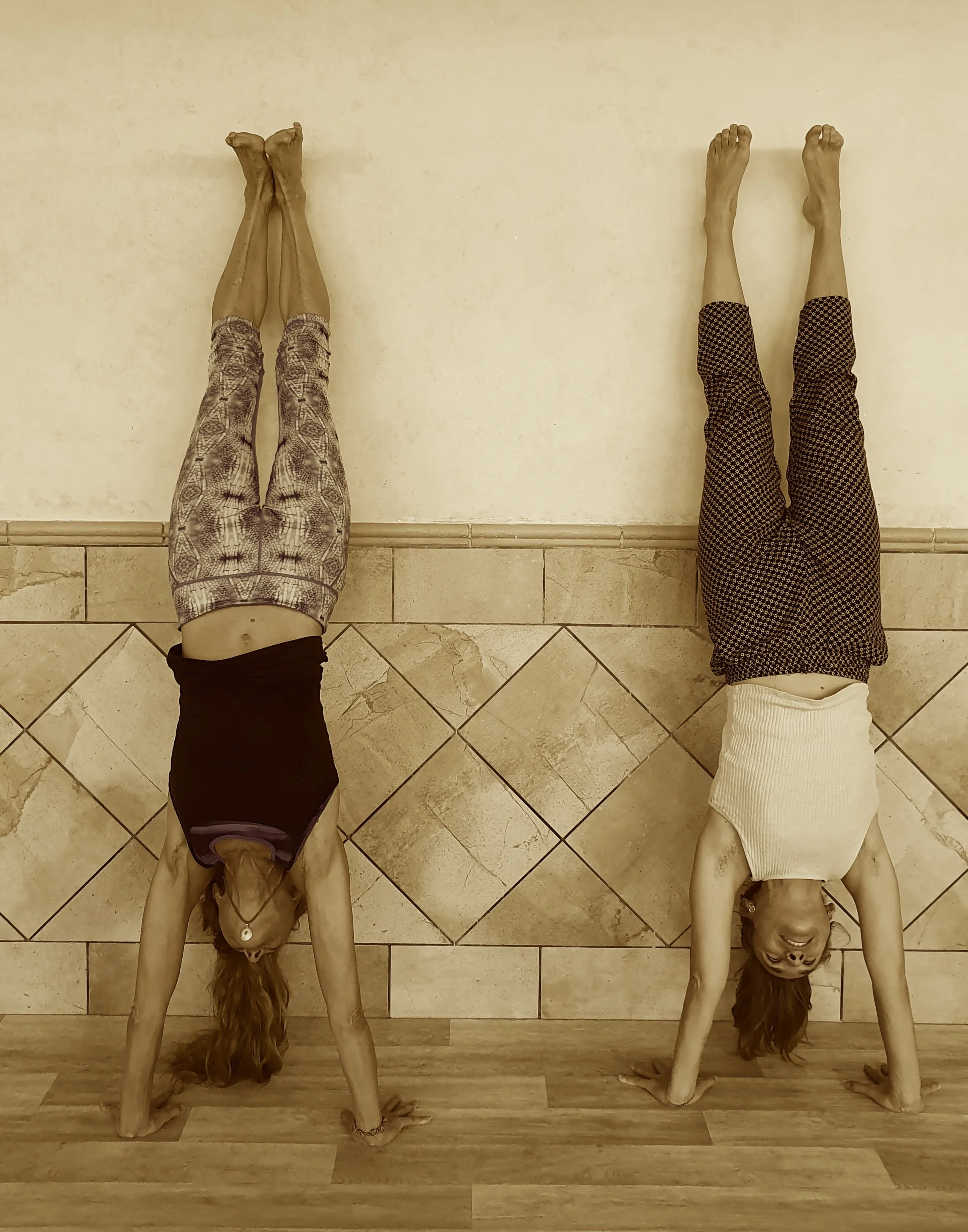 Two women lying on the floor with their legs against the wall, smiling and looking at the camera.