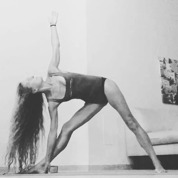 Woman practicing yoga in a room, with one hand and foot on the floor and the other arm extended upward in a pose.