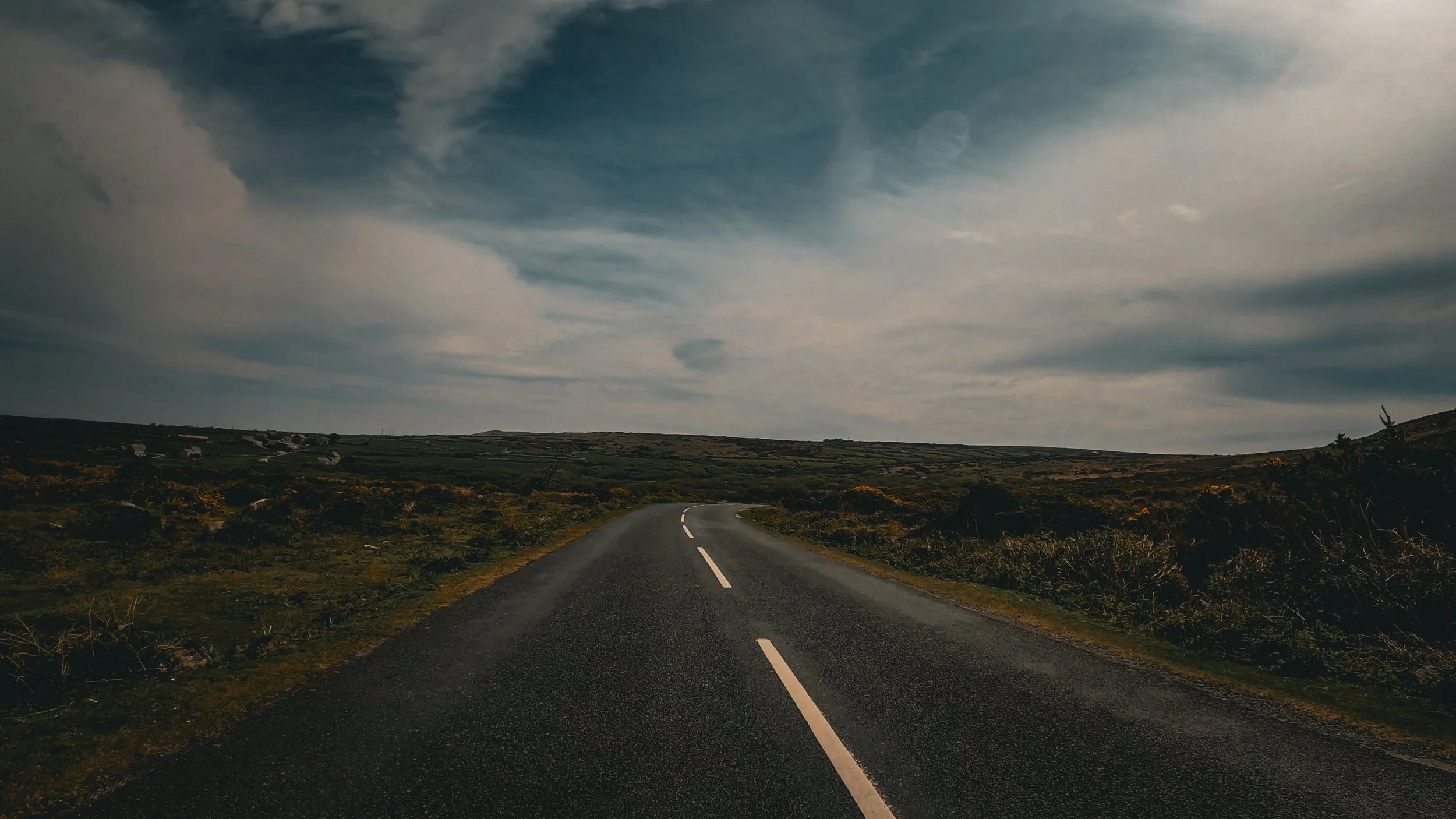 A winding road through a hilly landscape under a cloudy sky.