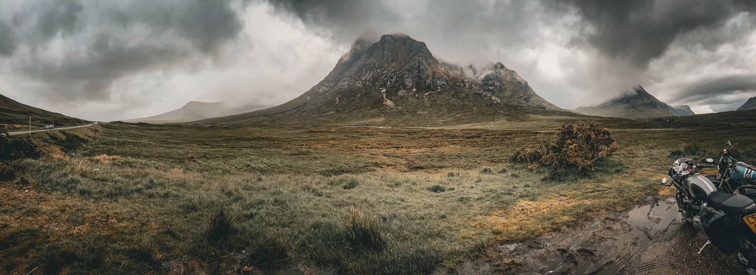 A rugged mountain landscape on a cloudy day with parked motorcycles in the foreground.