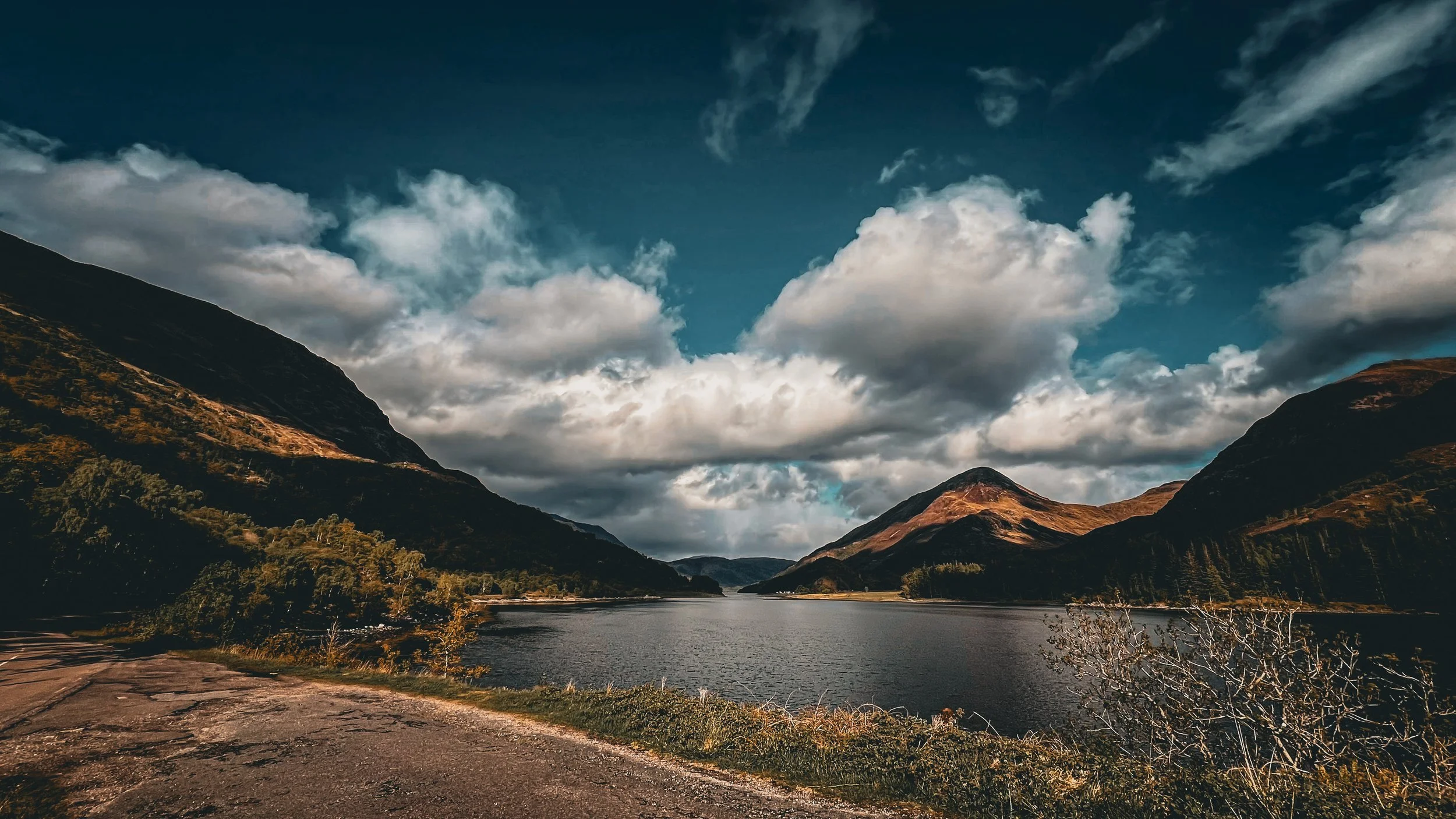 A scenic view of a lake surrounded by mountains under a partly cloudy sky.