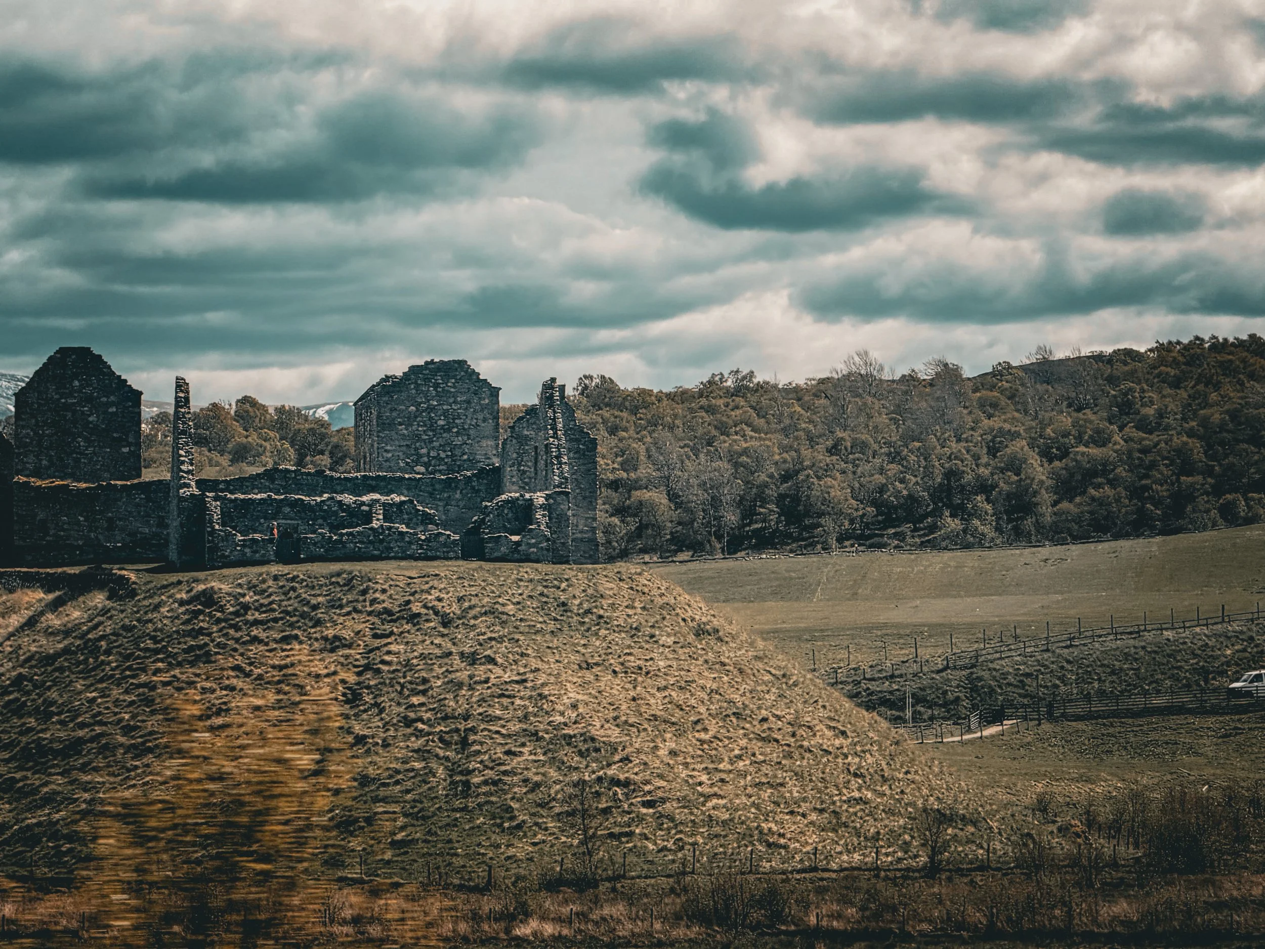 Ruins of an old stone building with a forest in the background and a cloudy sky overhead.