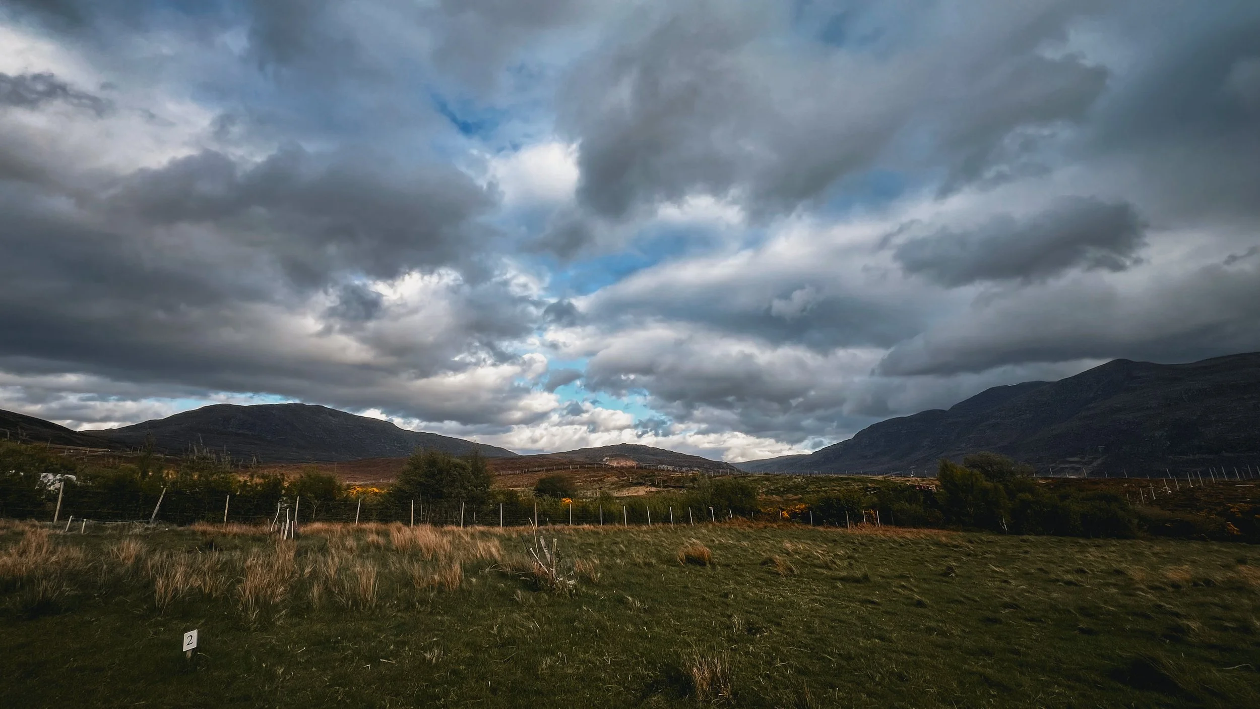 Landscape with rolling hills, mountains, and a cloudy sky with patches of blue.