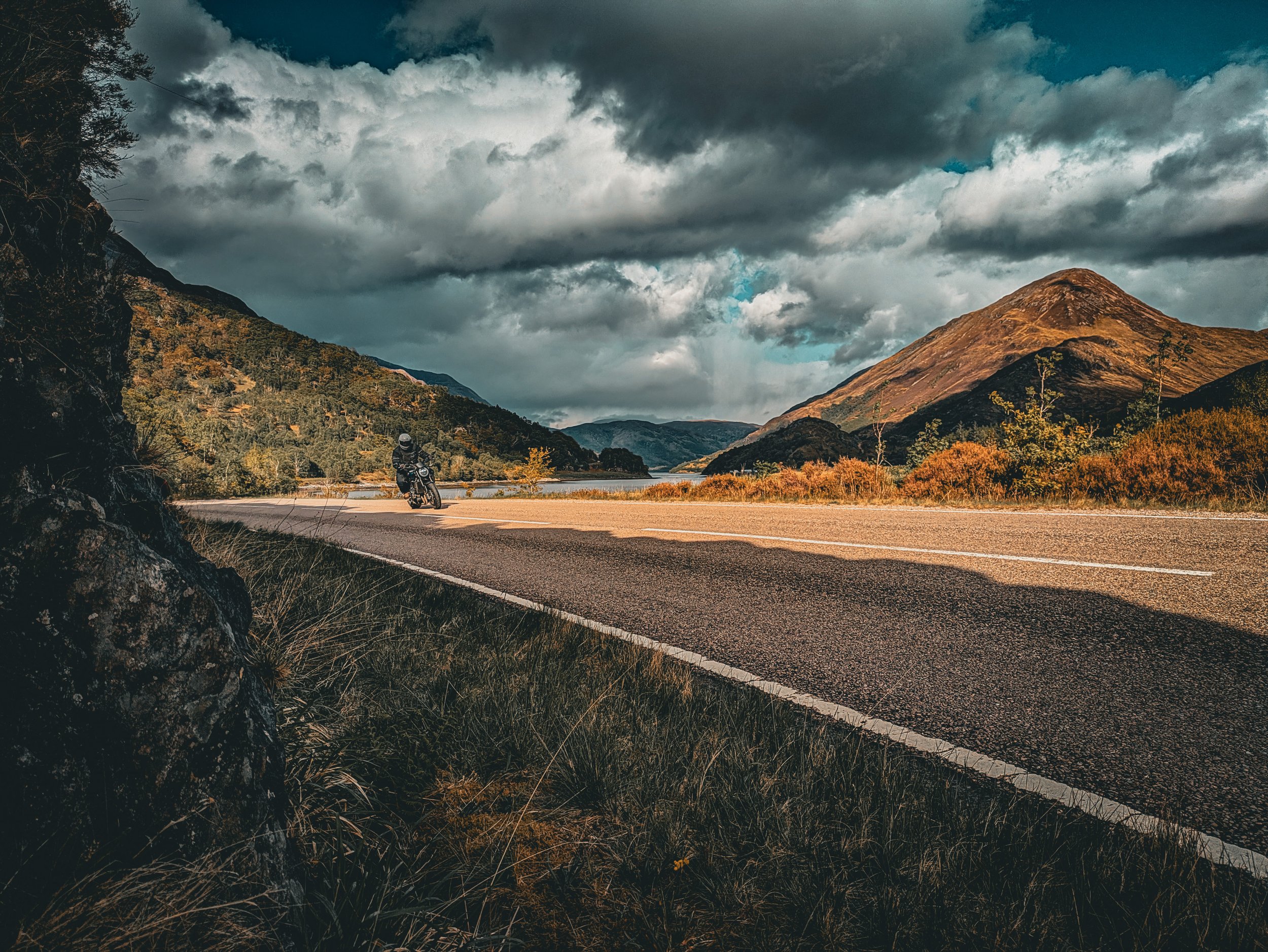 A person riding a motorcycle along a mountain road under a cloudy sky.