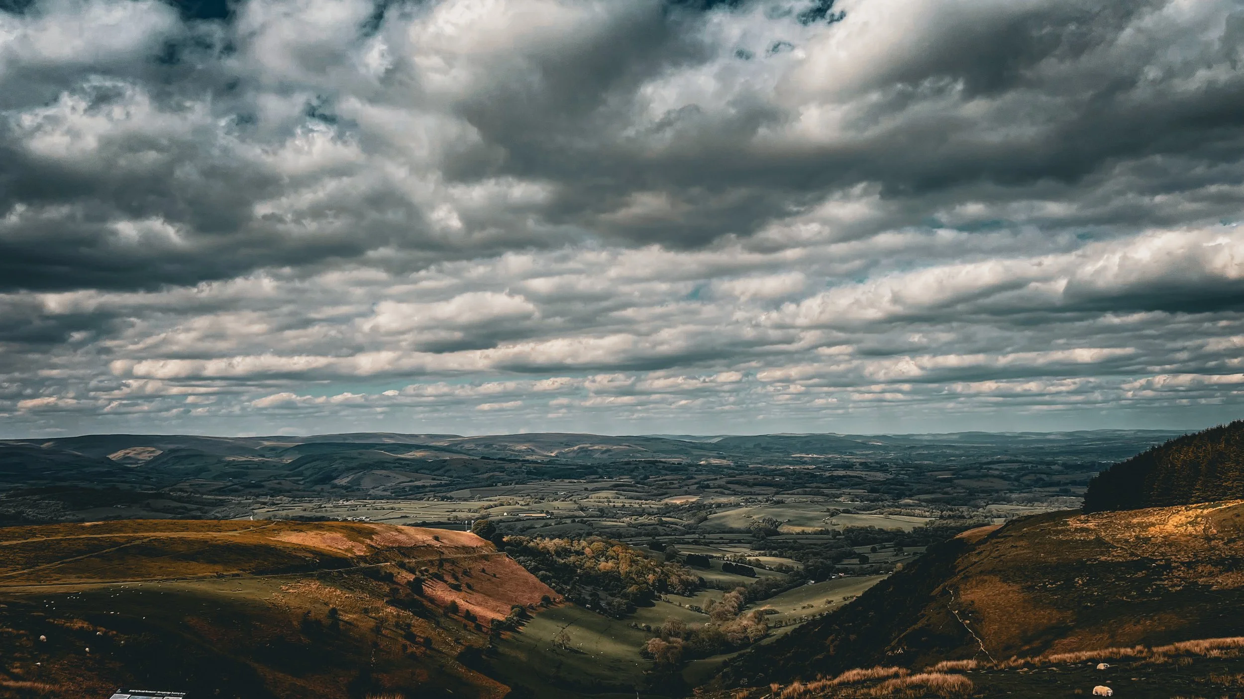 A scenic landscape with rolling hills and fields beneath a cloudy sky.