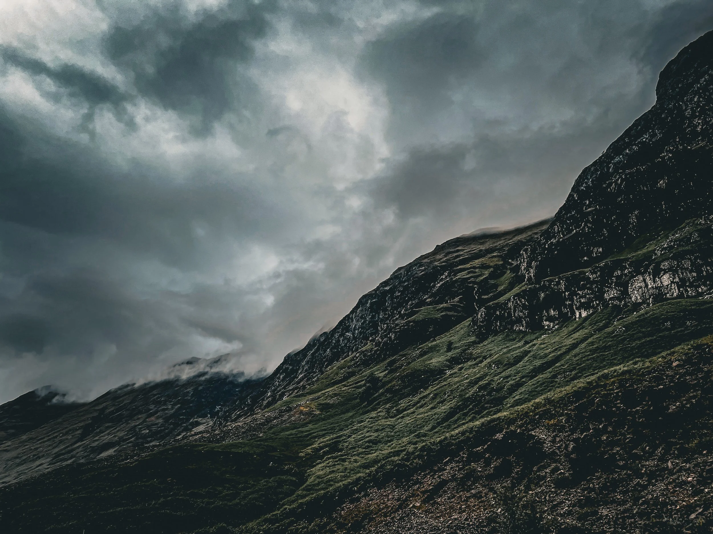 Dark stormy clouds over a rugged mountain landscape with patches of green grass.