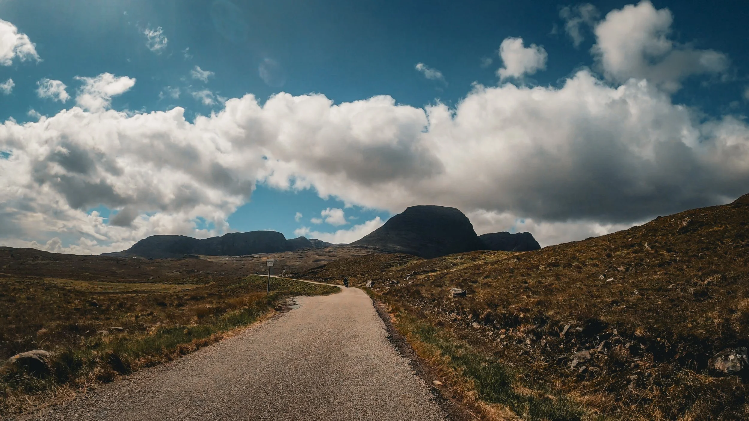 A winding dirt road in a mountainous landscape under a partly cloudy sky.