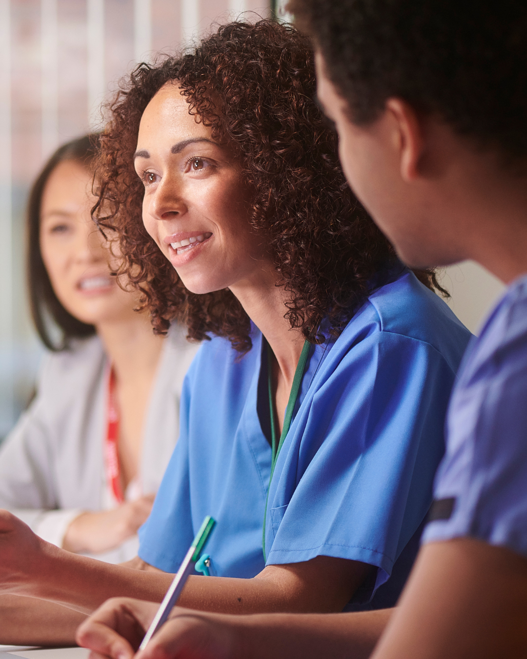 Three healthcare professionals, including a woman with curly hair in blue scrubs, engaged in a discussion or meeting.