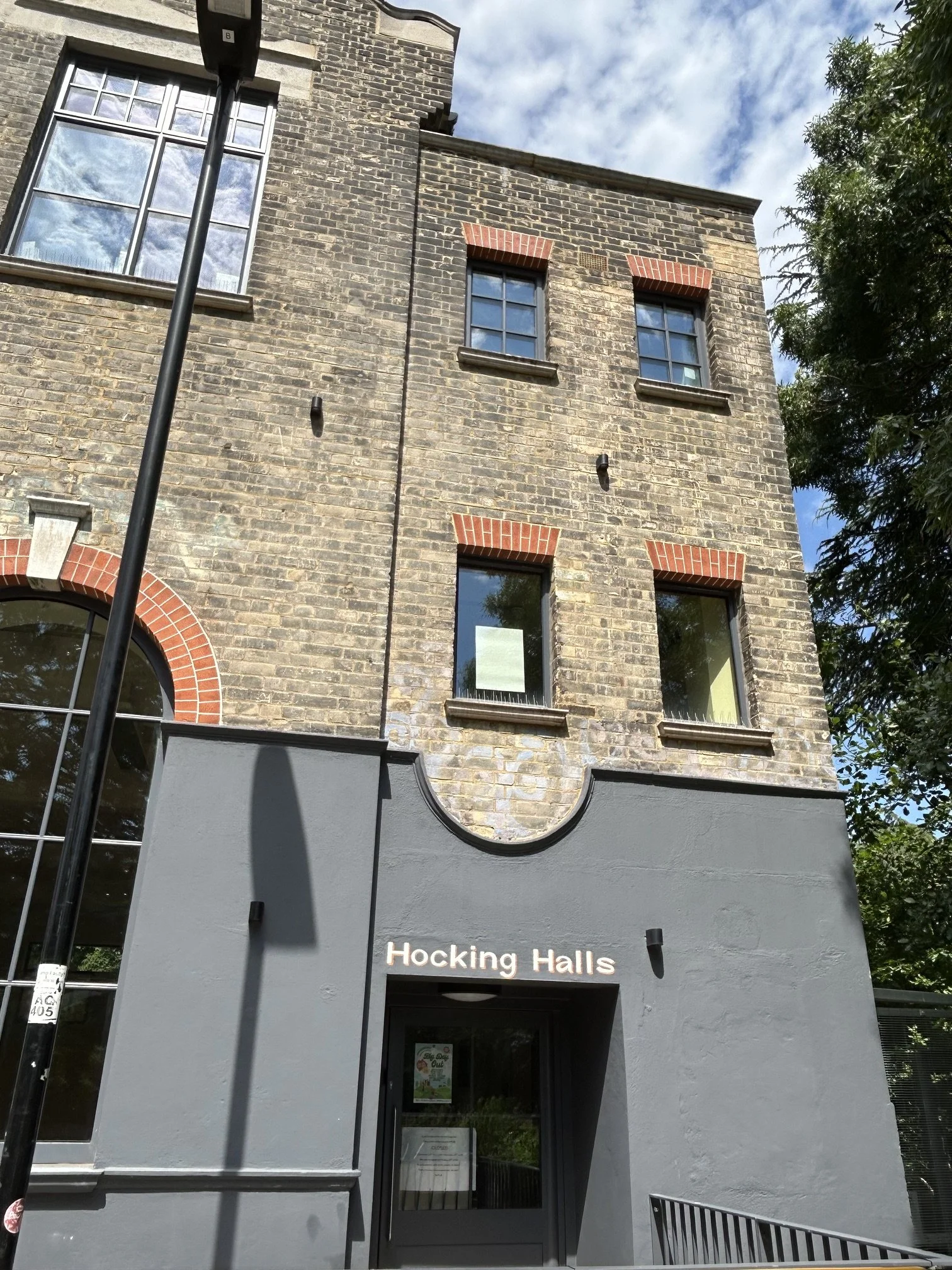 Front façade and new entrance of the Hocking Halls building in brickwork with large windows and a small clock on the upper part. Whittington Park Community Centre