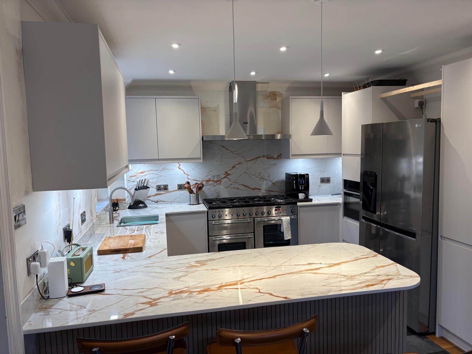 Modern kitchen with gray cabinets, stainless steel appliances including a fridge, oven, and coffee maker, marble countertops, and under-cabinet lighting. Wedmore House North Sommerset 