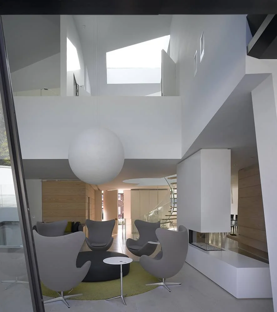 Modern living room with minimalist decor in a bright space with double high ceiling and lots of natural light. Egg chairs, Moon light by Davide Groppi, Dinesen boiserie and purpose made fireplace. Sheldon Avenue House, Hampstead.