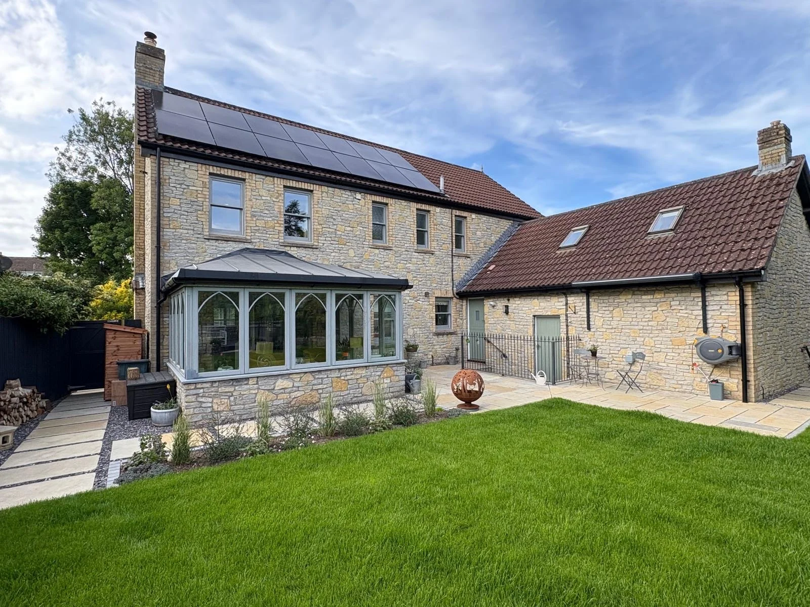 Rear view of a stone house with solar panels on the roof, a small porch, a well-maintained lawn, and outdoor furniture. Wedmore House North Sommerset 