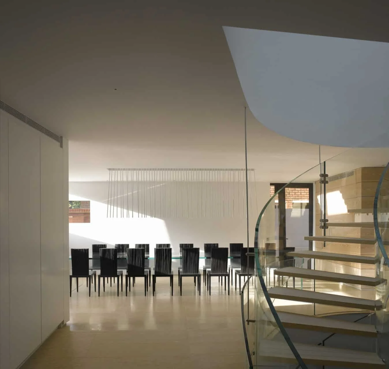 Modern living room with minimalist décor, glass staircase by Santambrogio Milano, large dining table with Viabizzuno  light above. Natural marble floor from Carrara. Sheldon Avenue House, Hampstead.