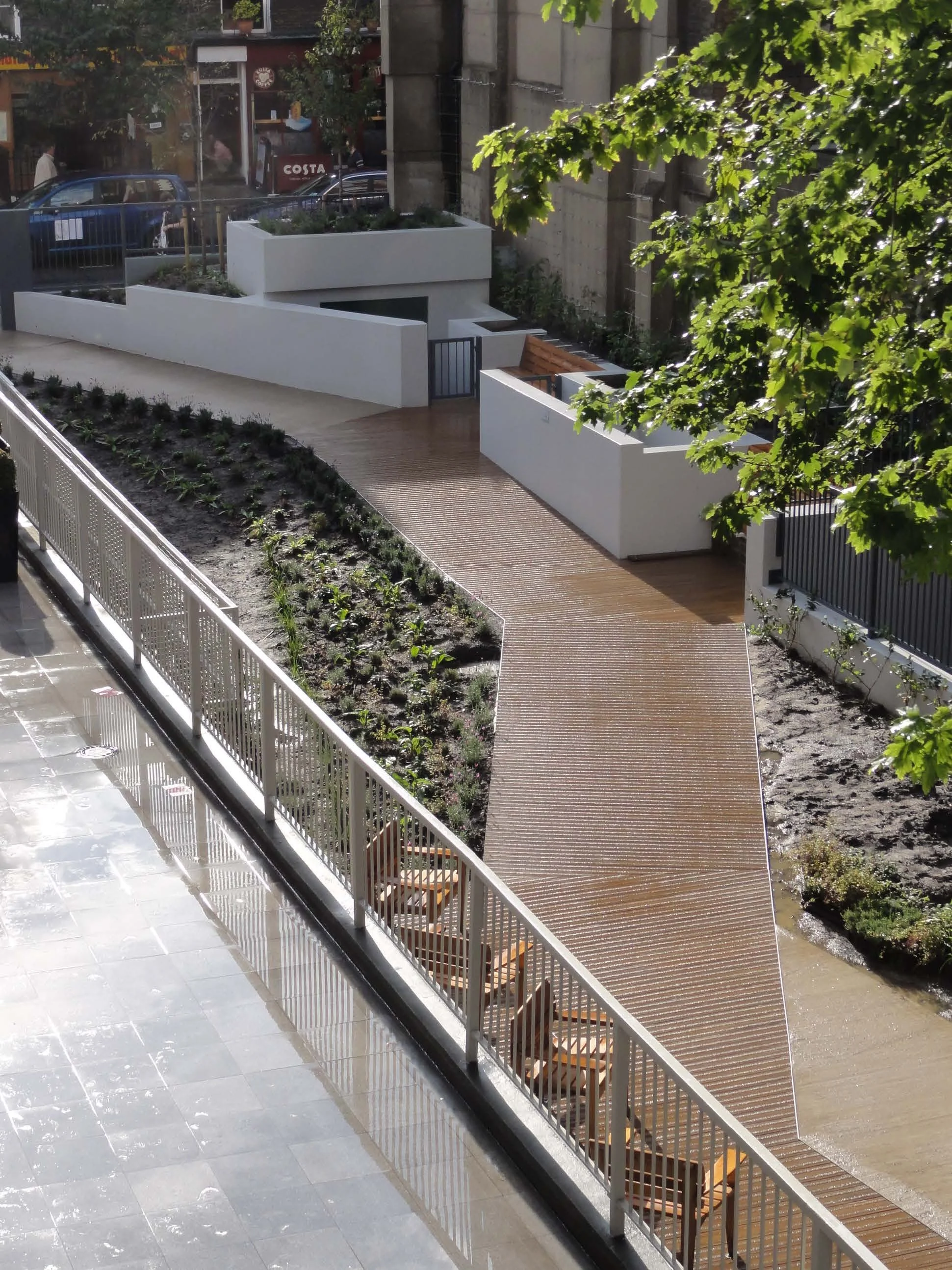 View of the garden connecting Marchmont Street to Kenton Street with the central section of the garden with the Millboard decking wooden and the white painted walls around the existing gas stores. Marchmont Street Community Gardens
