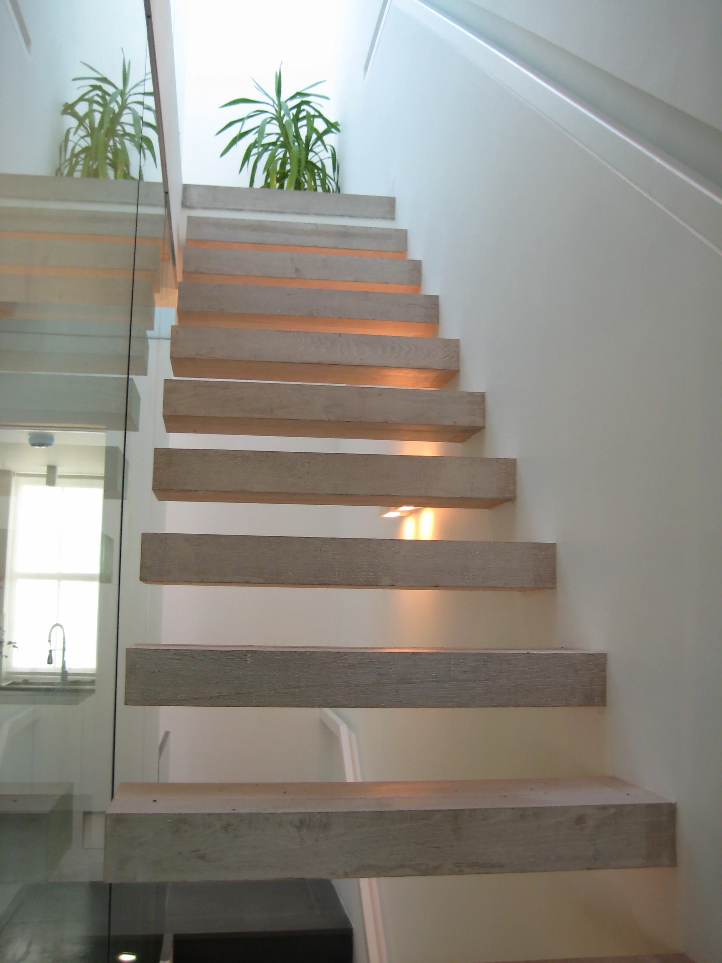 Interior view of a staircase with light-colored wooden steps, a glass side panel to access the large roof terrace. South Kensington House