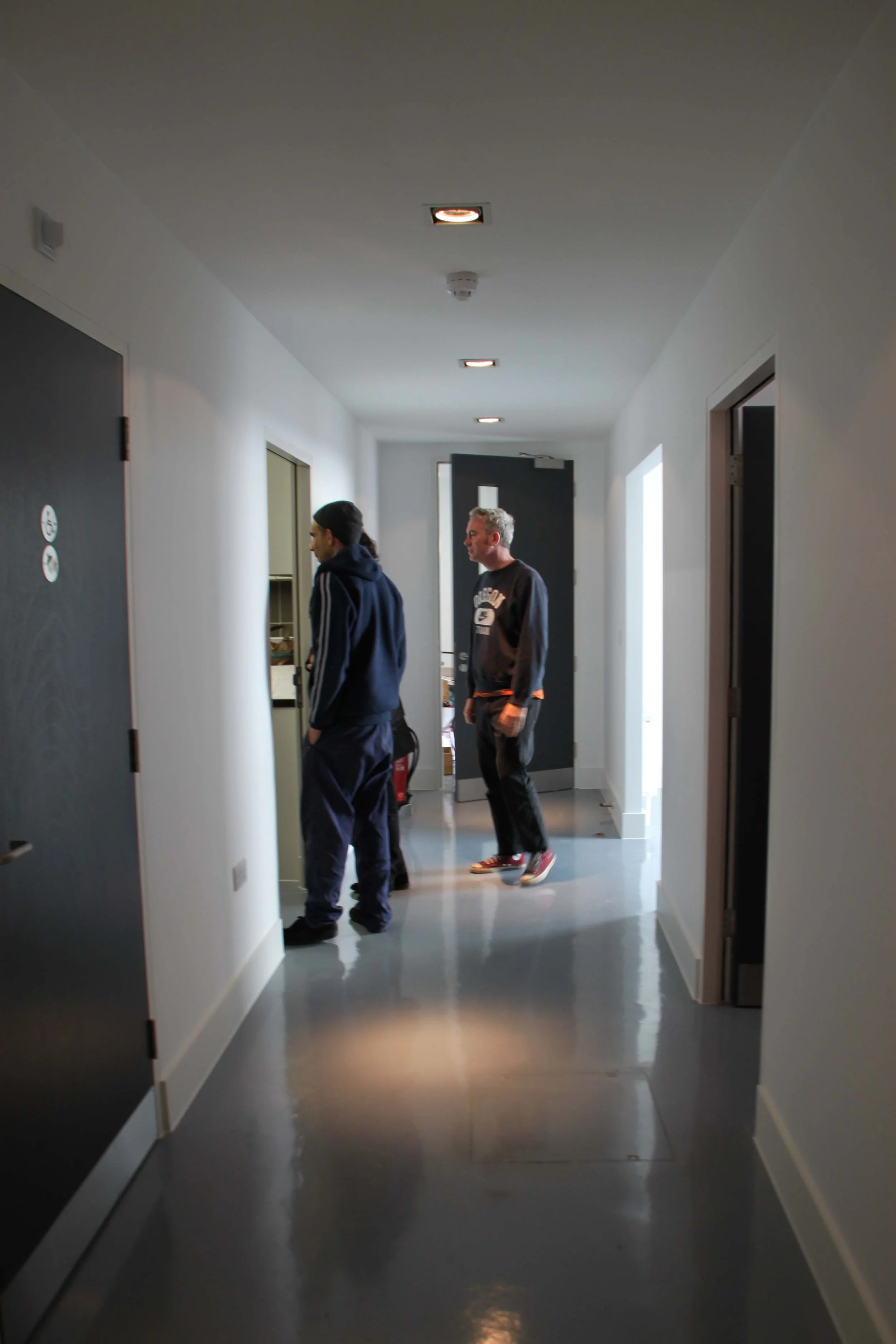 First Floor hallway with white walls, black doors, and ceiling lights. Sparkplug