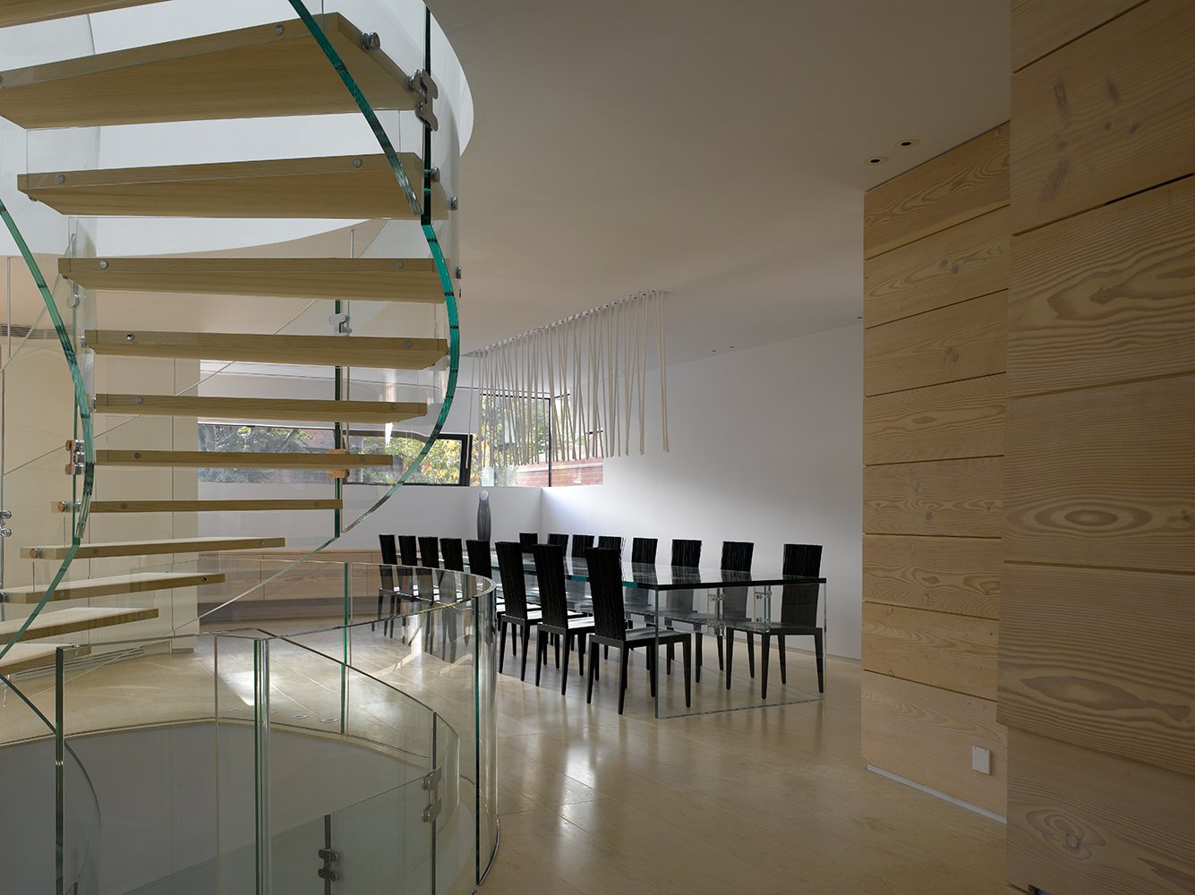 Modern dining room with minimalist décor, glass staircase by Santambrogio Milano, large dining table with Viabizzuno  light above, Dinesen boiserie and marble floor from Carrara. Sheldon Avenue House, Hampstead.