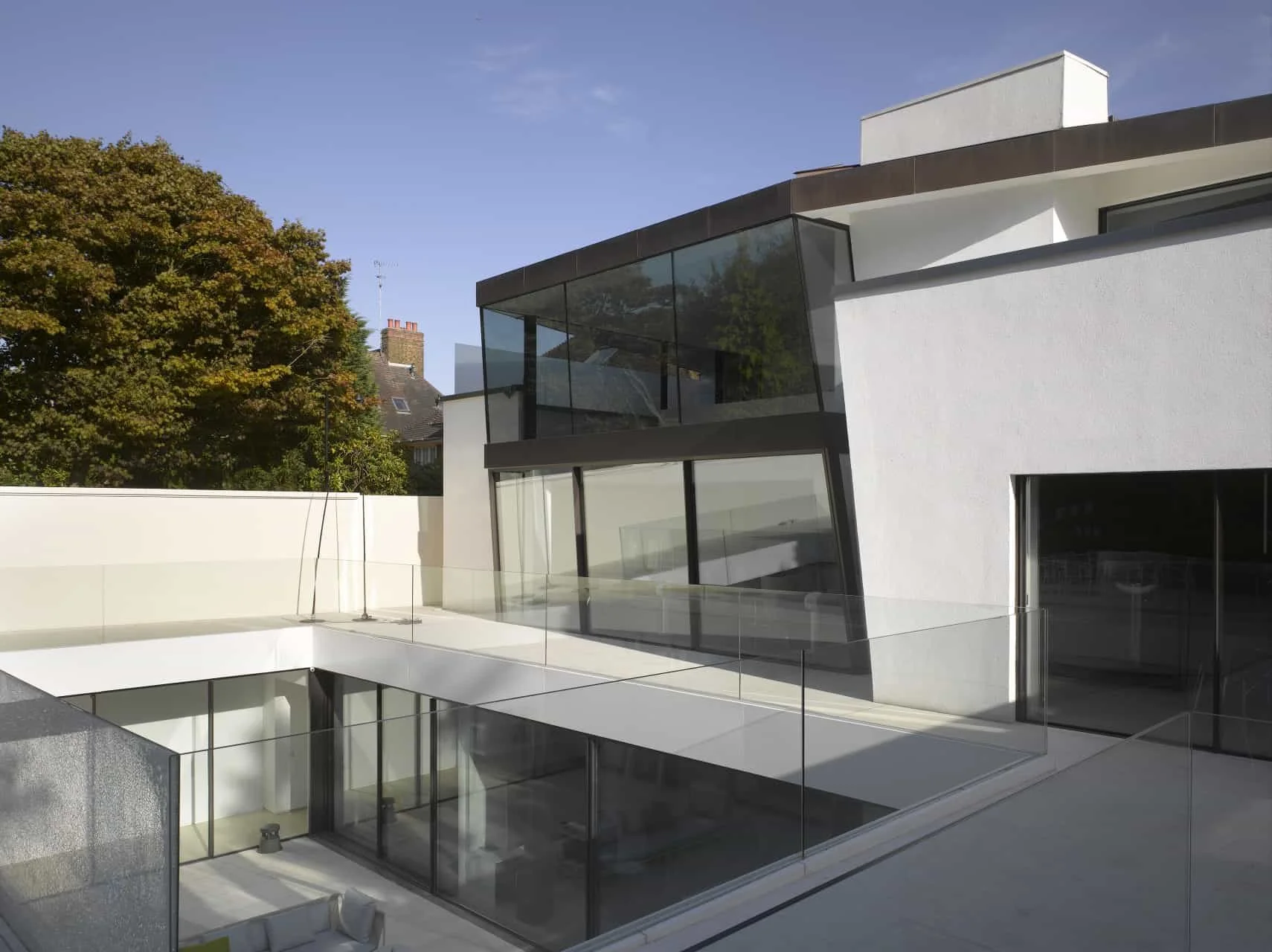 Rear façade of the modern white building with extensive glass windows and a balcony. Sheldon Avenue House, Hampstead.