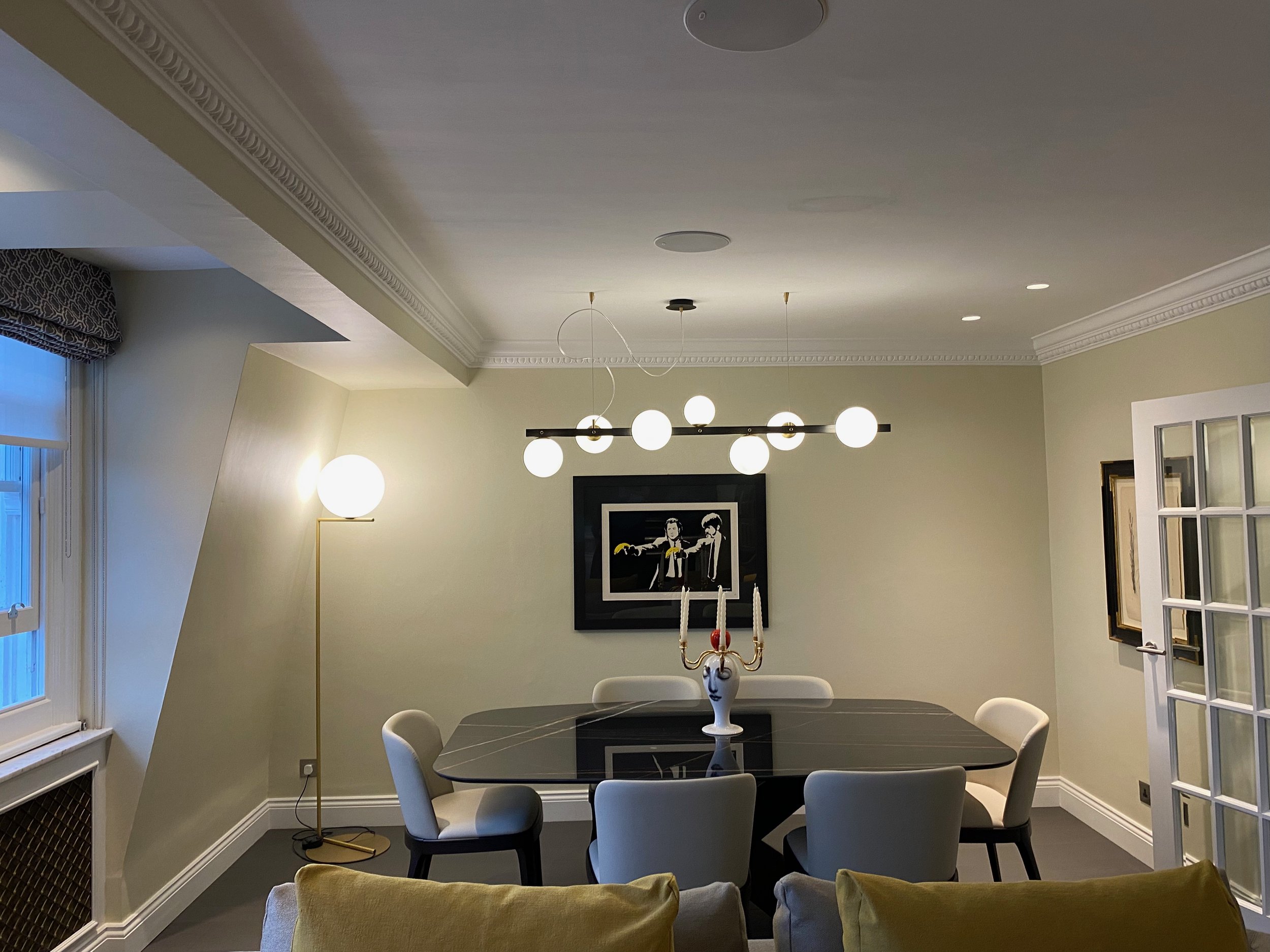 Dining room with a black marble table, white chairs, a chandelier with white globes, and framed artwork on the wall. Pont Street Knightsbridge 