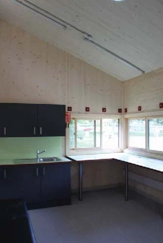 Kitchen with black cabinets, a windowed corner, a countertop, and a ceiling with exposed structural elements. Whittington Park Sport Pavilion