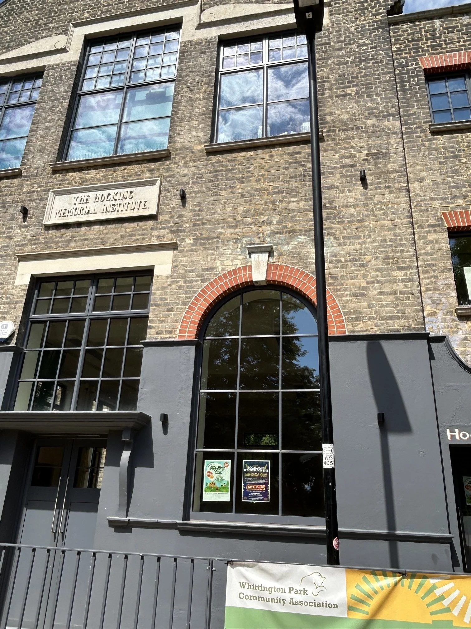 Front façade and new entrance of the Hocking Halls building in brickwork with large windows and a small clock on the upper part. Whittington Park Community Centre