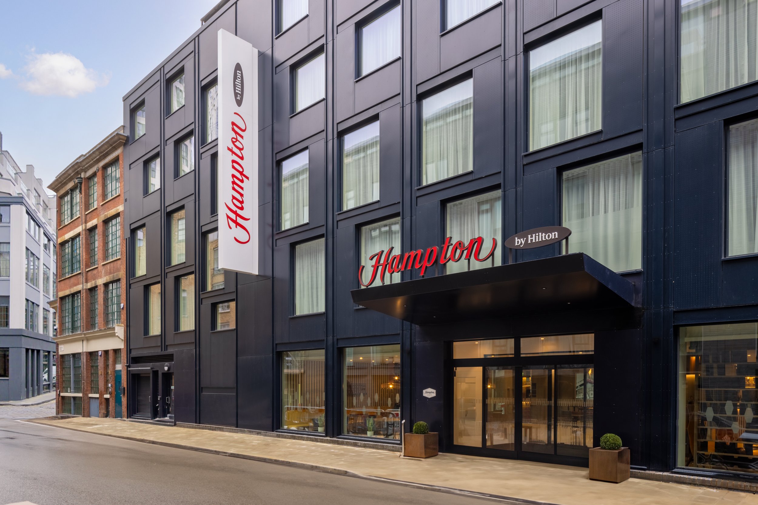 Street view of the new Hampton by Hilton Hotel in Old Street finish in dark blue metal panels with large windows.