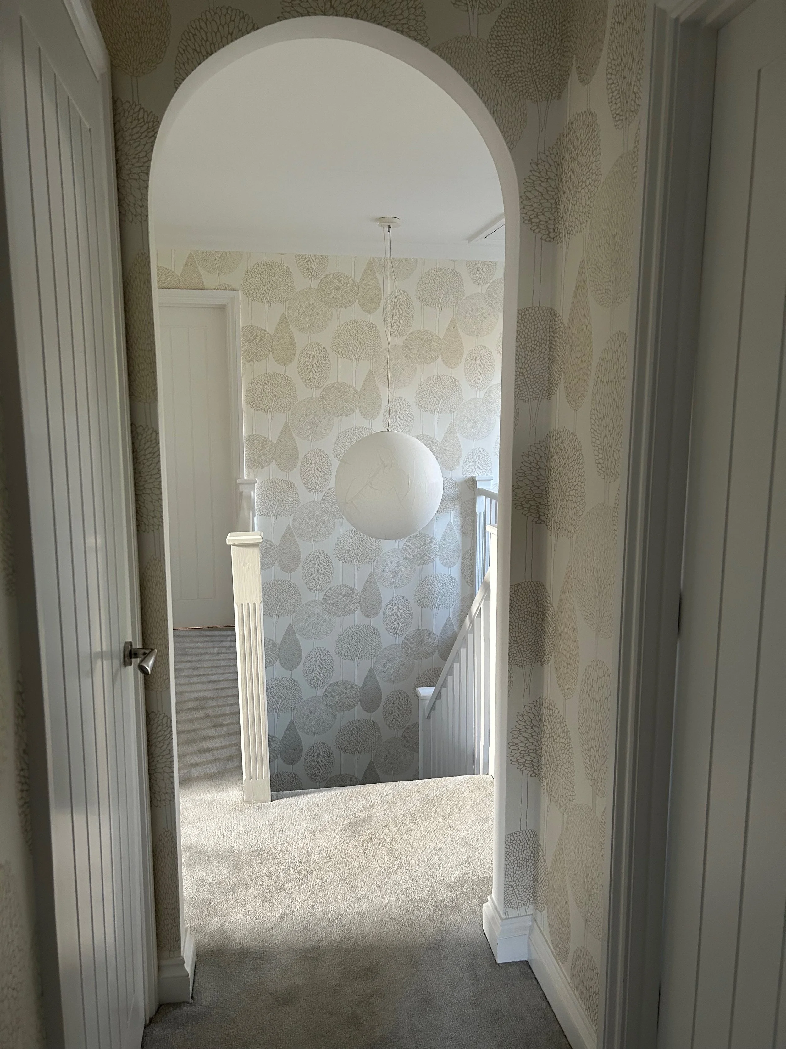 Hallway leading to a staircase with beige carpet, framed by wallpaper with tree patterns, and a pendant Moon light by Davide Groppi. Wedmore House North Sommerset 